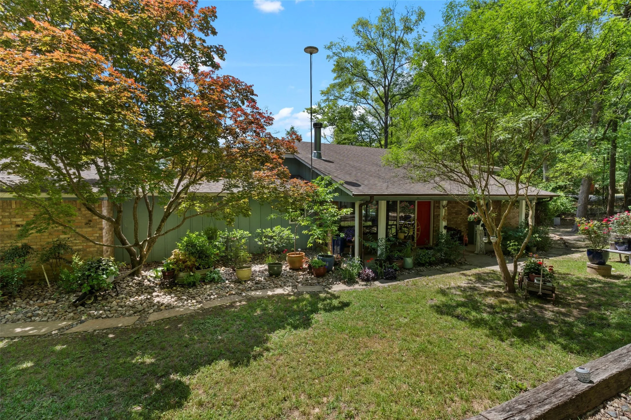 Ranch-style exterior featuring a covered porch, brick facade, and a red entry door