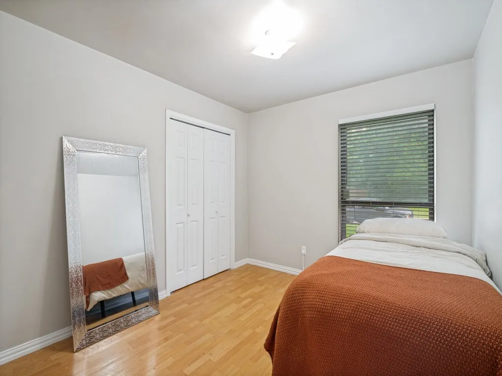 Bedroom featuring light wood-finish flooring, a double-door closet with bifold doors, a window with horizontal blinds, and a flush-mount ceiling light fixture