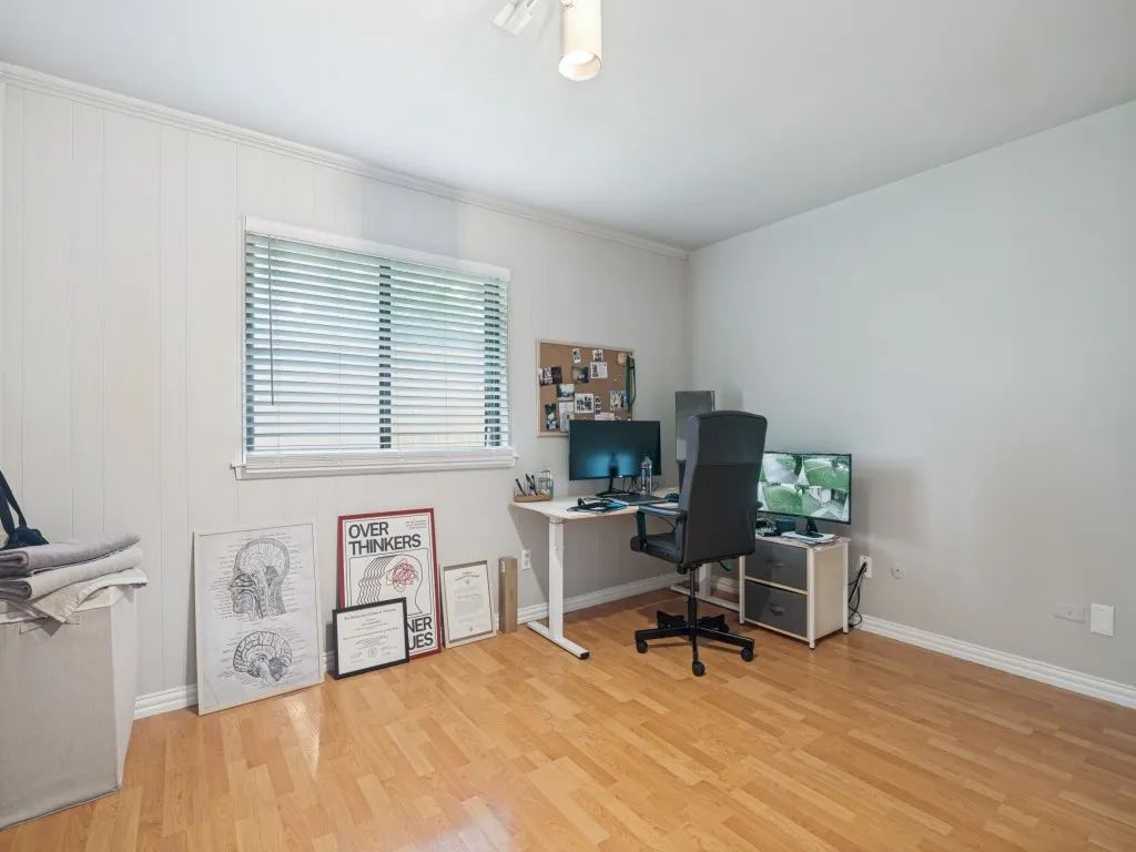 Room featuring wood-finish flooring, white paneling on one wall, a window with blinds, and white baseboards