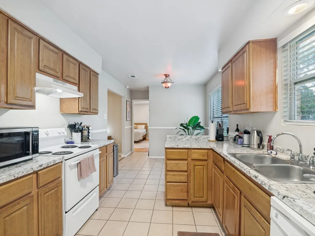 Kitchen featuring wood cabinetry, light-toned countertops, a double basin sink, and tile flooring