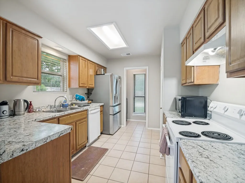 Galley kitchen featuring wood cabinetry, light-toned countertops, a double basin sink, and tile flooring