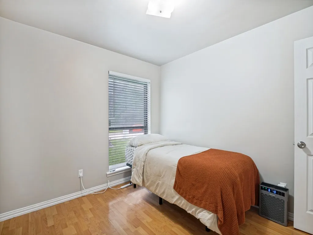 Room featuring wood-finish flooring, a window with horizontal blinds, light-colored walls, white trim, and an overhead flush-mount light fixture