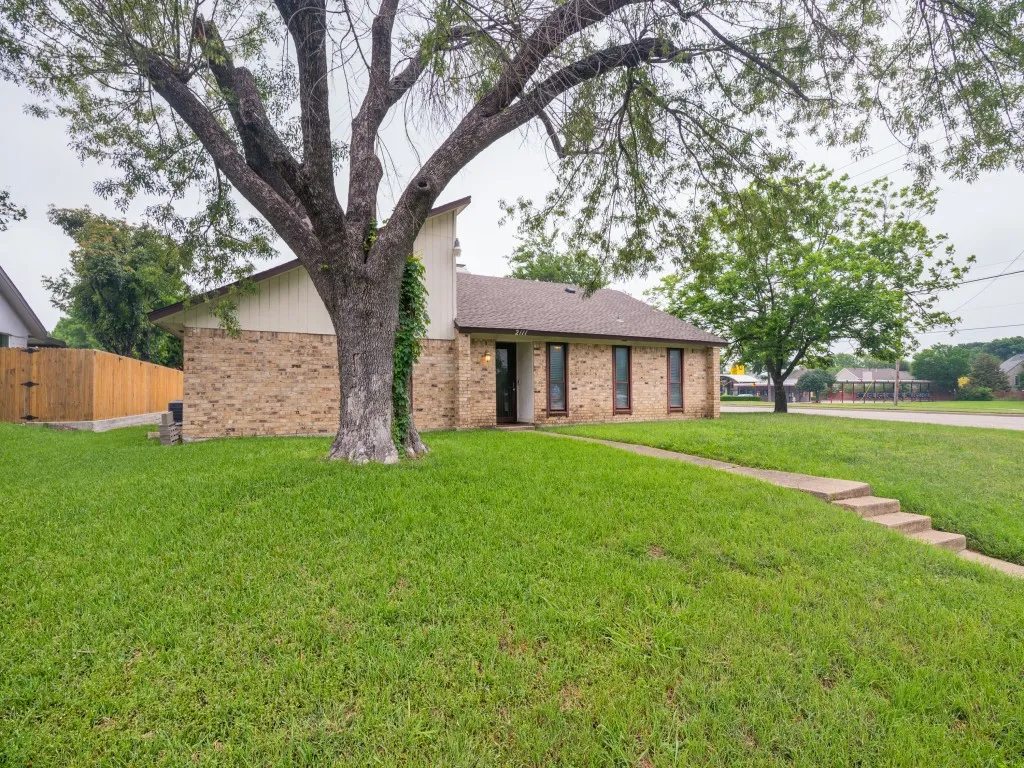 Brick and siding exterior featuring a prominent mature tree, a neatly maintained lawn, and a multi-step concrete walkway