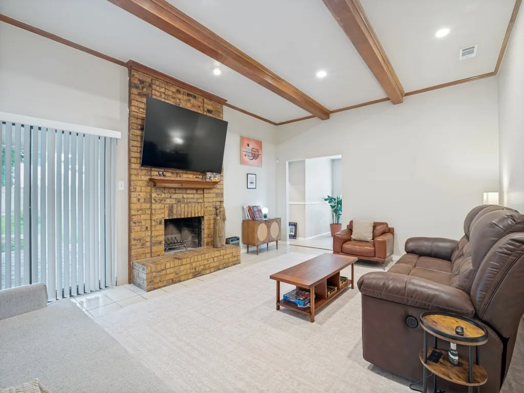 Living area featuring a floor-to-ceiling brick fireplace with a wood mantle, vaulted ceiling with exposed wood beams, recessed lighting, and tile flooring