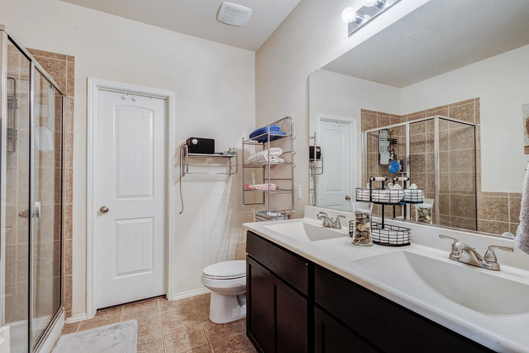 Bathroom featuring a double vanity with integrated sinks, a large wall-mounted mirror, a separate shower enclosure with a glass door, and tiled flooring