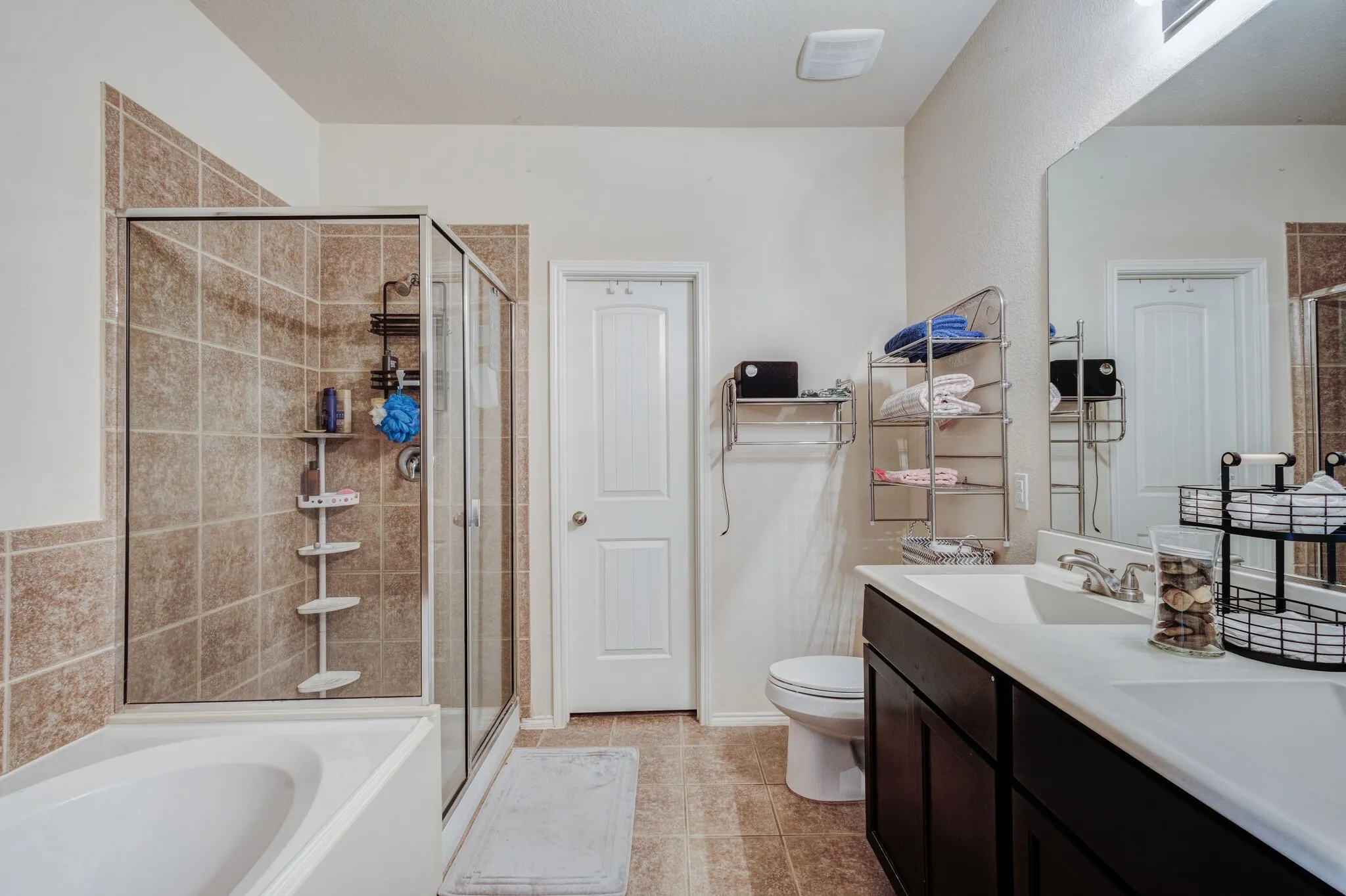 Bathroom featuring a glass-enclosed shower with tile surround, a built-in bathtub, a double vanity with an integrated sink, a large mirror, and tiled flooring