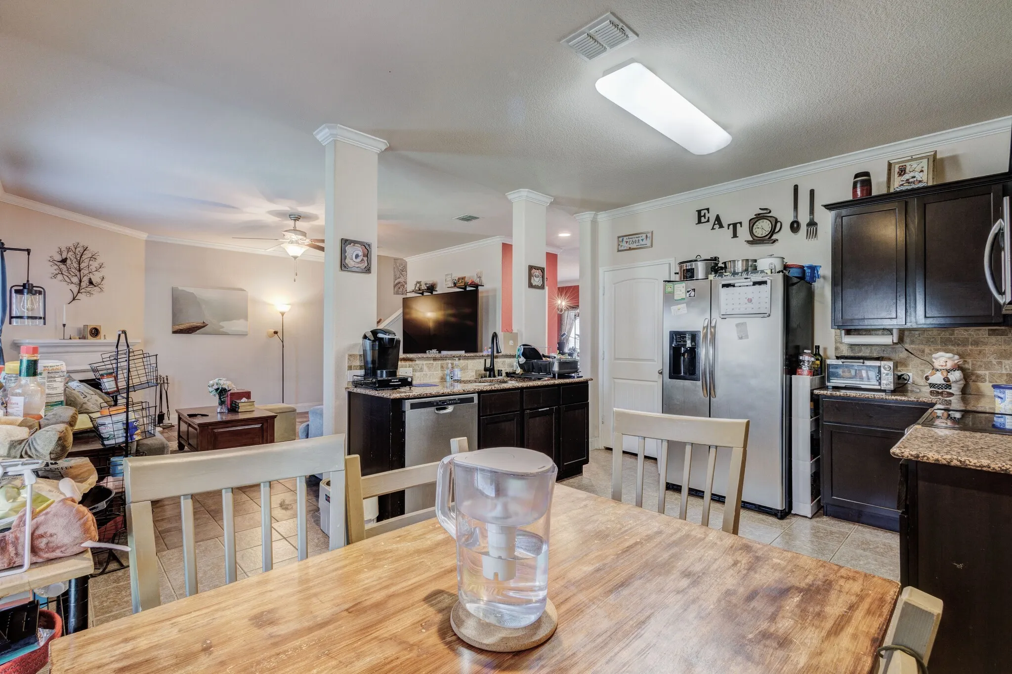 Open-concept kitchen and dining area featuring dark wood-finish cabinetry, stainless steel appliances, and a tiled backsplash