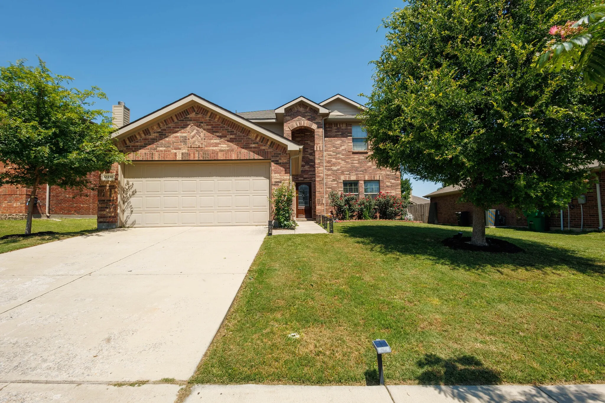 Brick exterior with a two-car garage, concrete driveway, and established landscaping