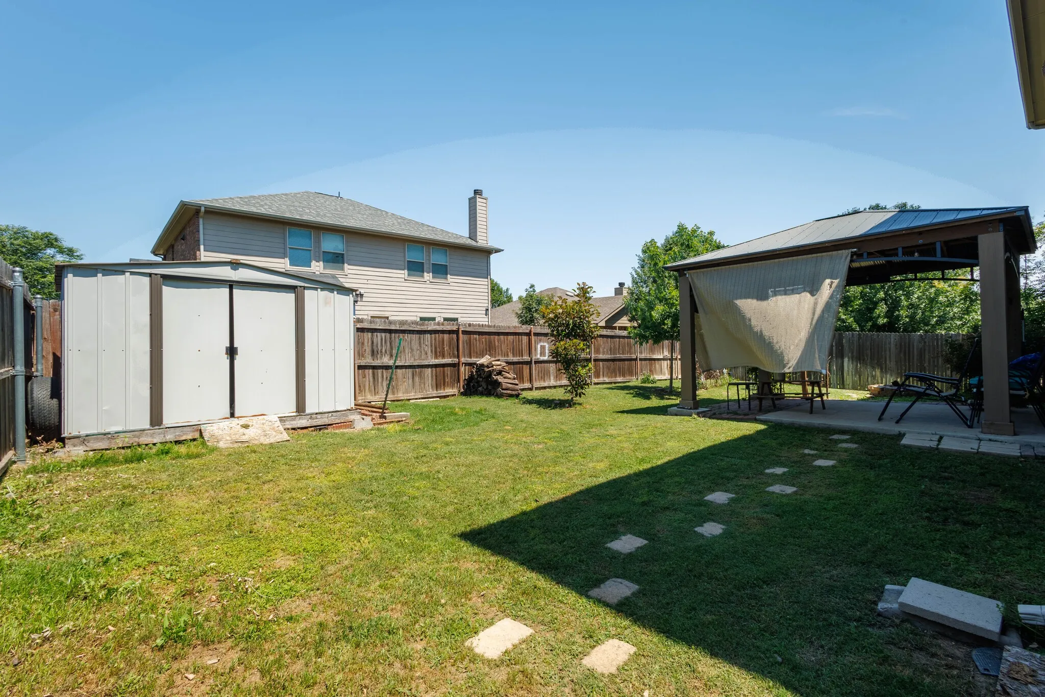 Spacious backyard featuring a metal storage shed, a covered patio structure with a concrete slab, and a wood privacy fence