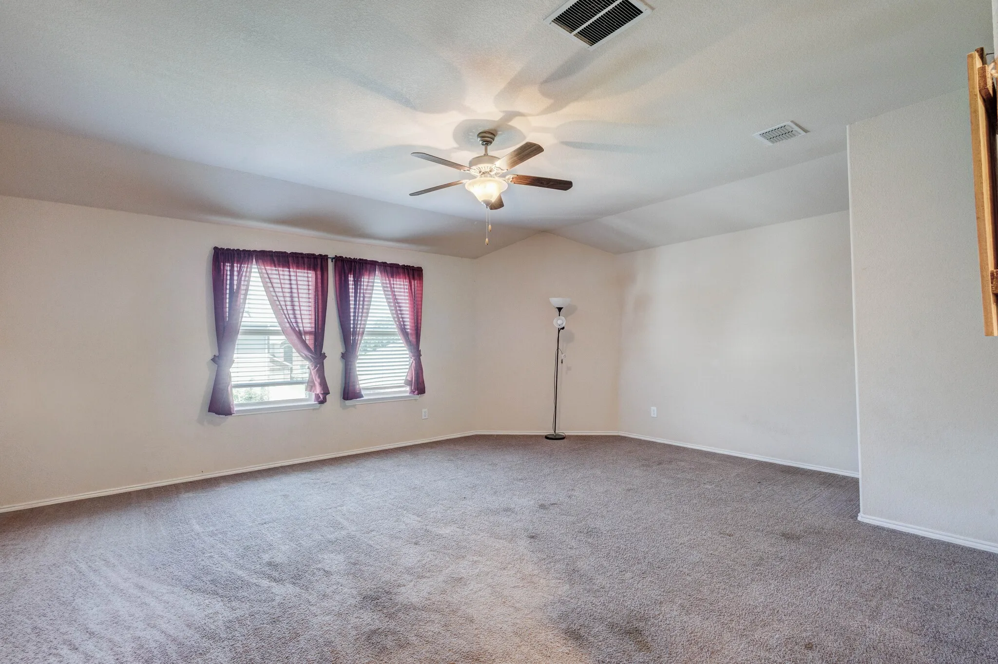 Spacious room featuring vaulted ceilings, two windows with blinds, a ceiling fan with integrated lighting, and neutral-toned carpeting