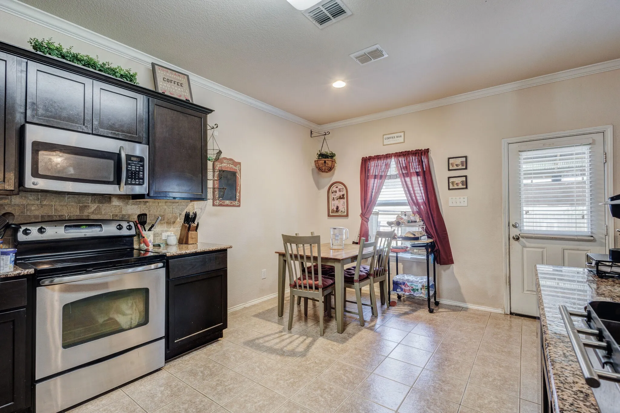Kitchen featuring dark wood cabinetry, stainless steel appliances, stone-look countertops, and tile flooring