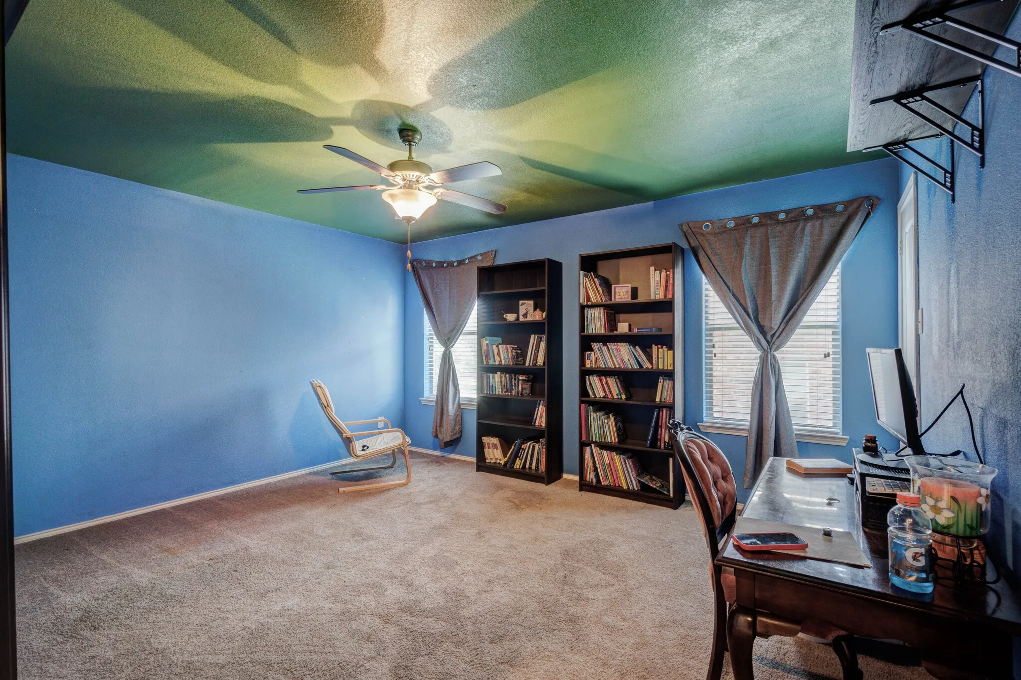 Spacious interior room featuring plush carpet flooring, multiple windows with blinds, built-in shelving, and a ceiling fan with integrated lighting
