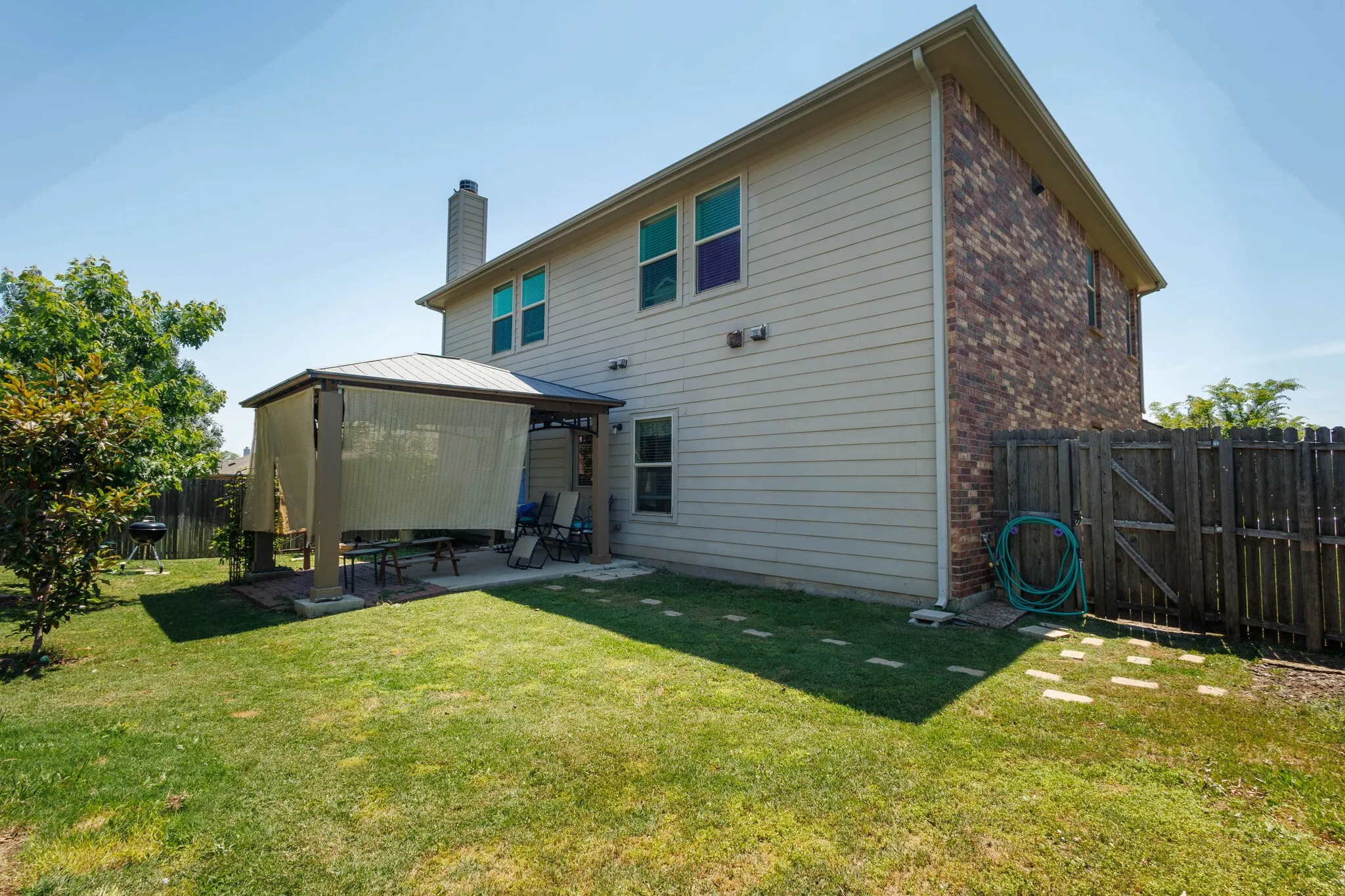 Expansive backyard featuring a covered patio with shade screens, a manicured lawn, and a privacy fence