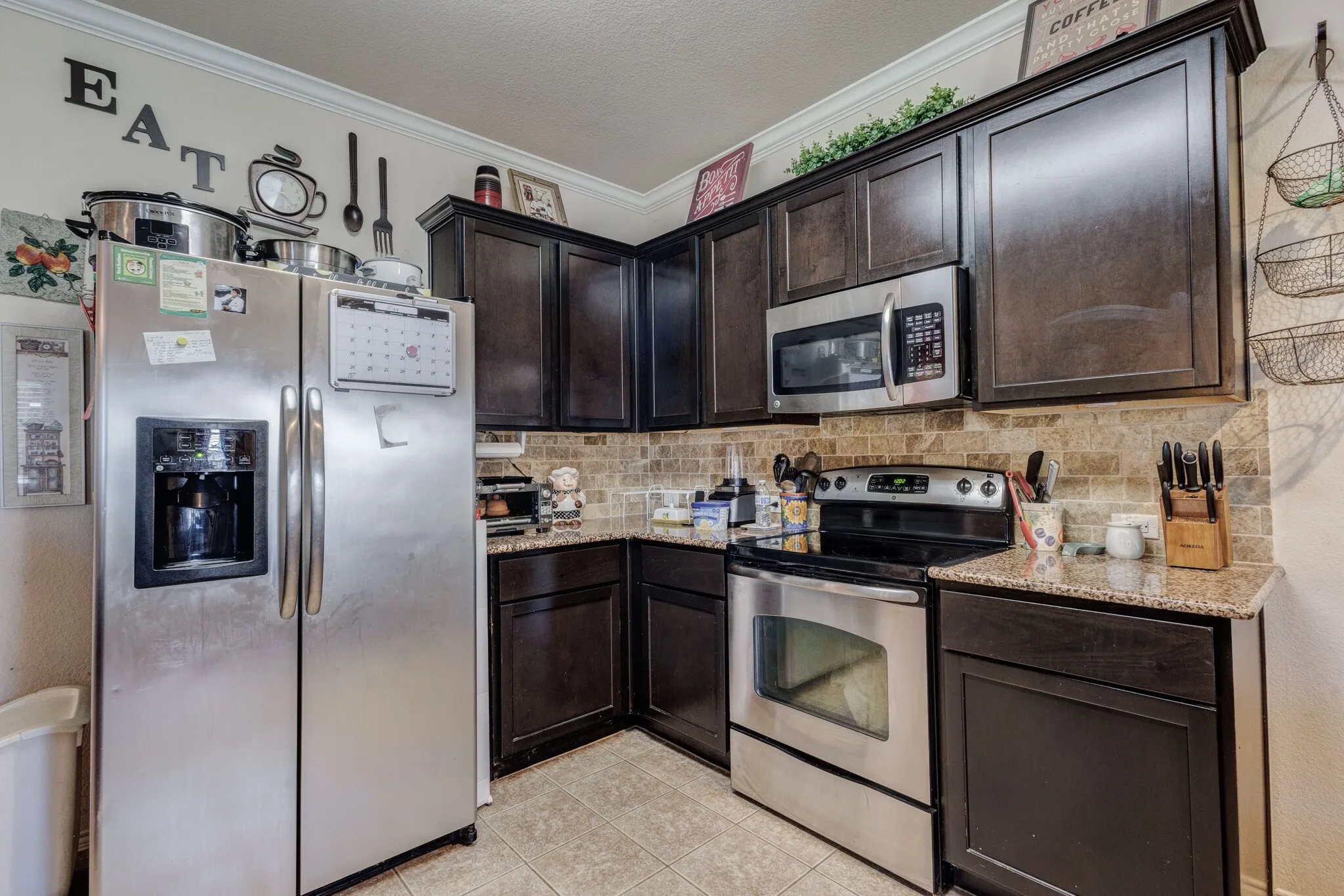 Kitchen featuring dark wood cabinetry, granite countertops, stainless steel appliances, a tile backsplash, and light-toned tile flooring