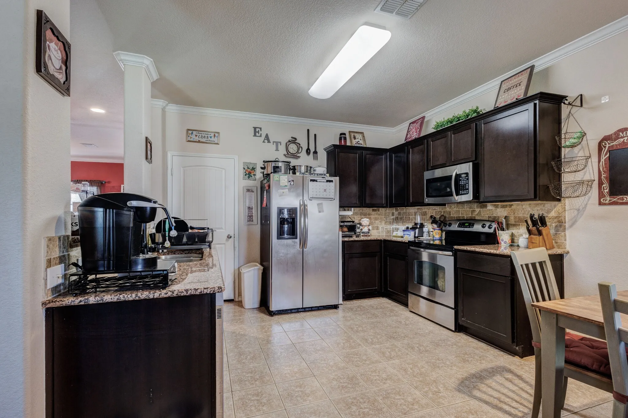Kitchen featuring dark wood cabinetry, light granite-style countertops, and a tiled backsplash