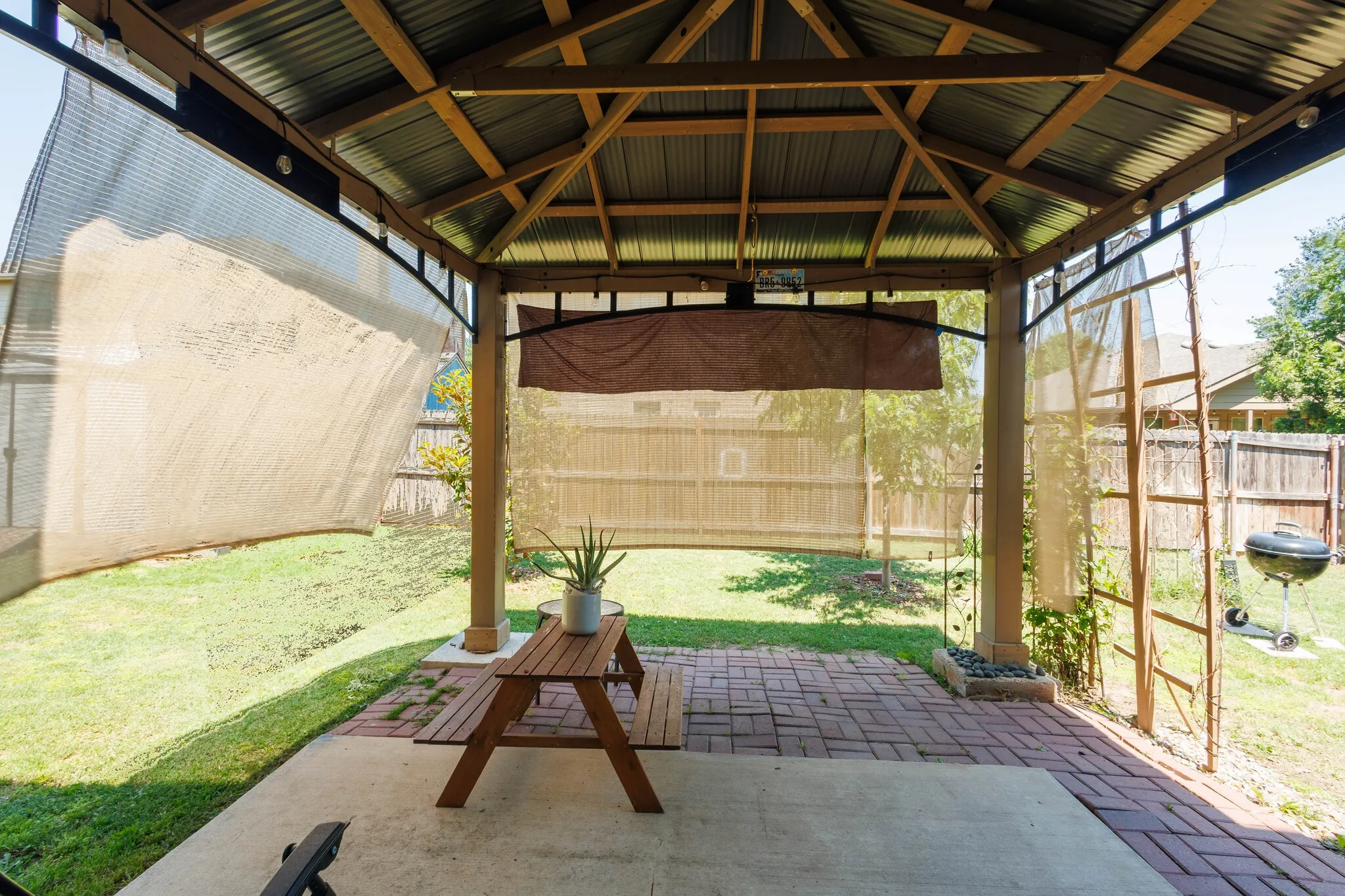 Backyard gazebo featuring a corrugated metal roof, wood beam construction, and integrated sun shades