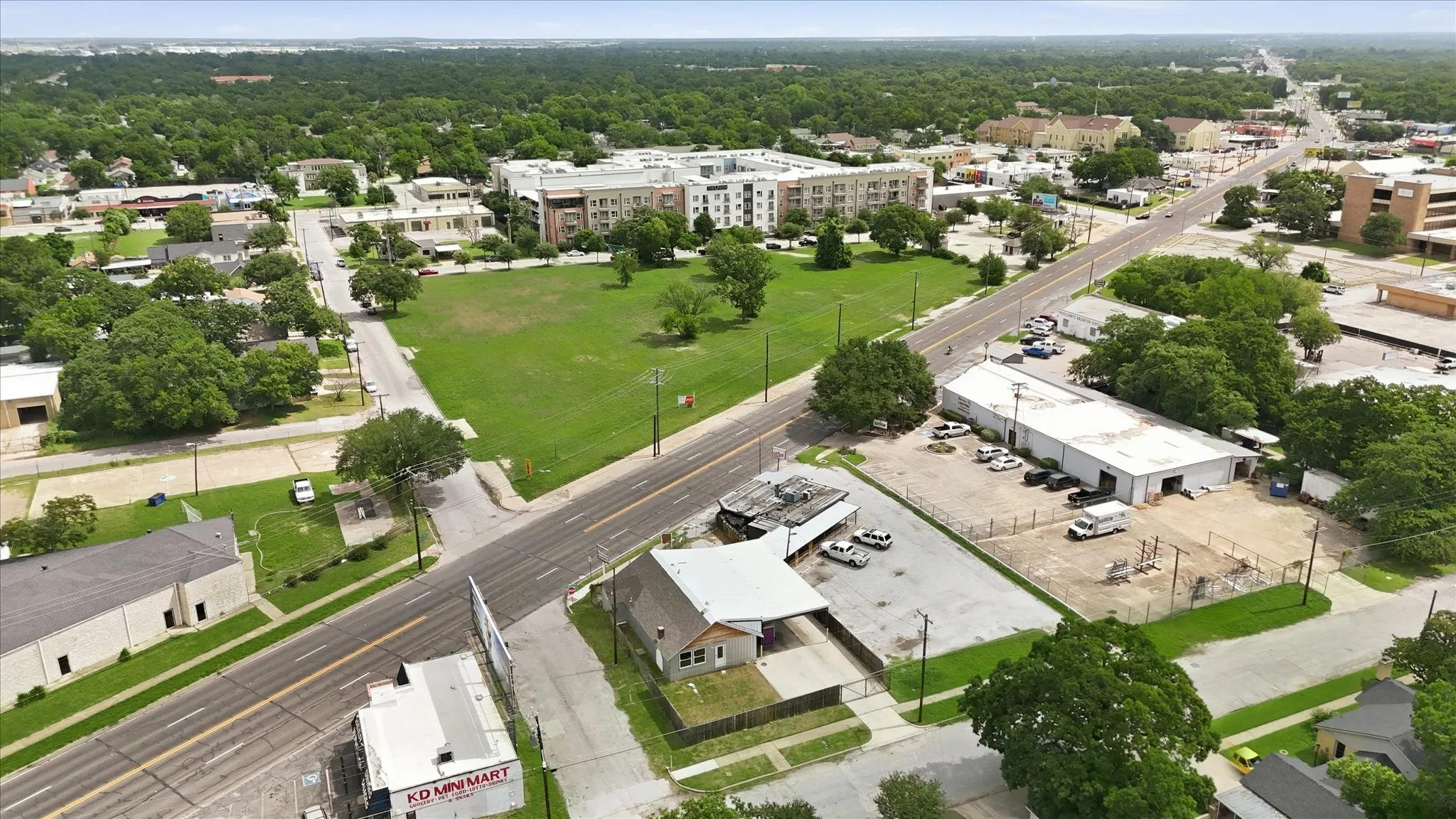 Expansive parcel featuring a commercial building with an attached carport, paved parking areas, and mature trees