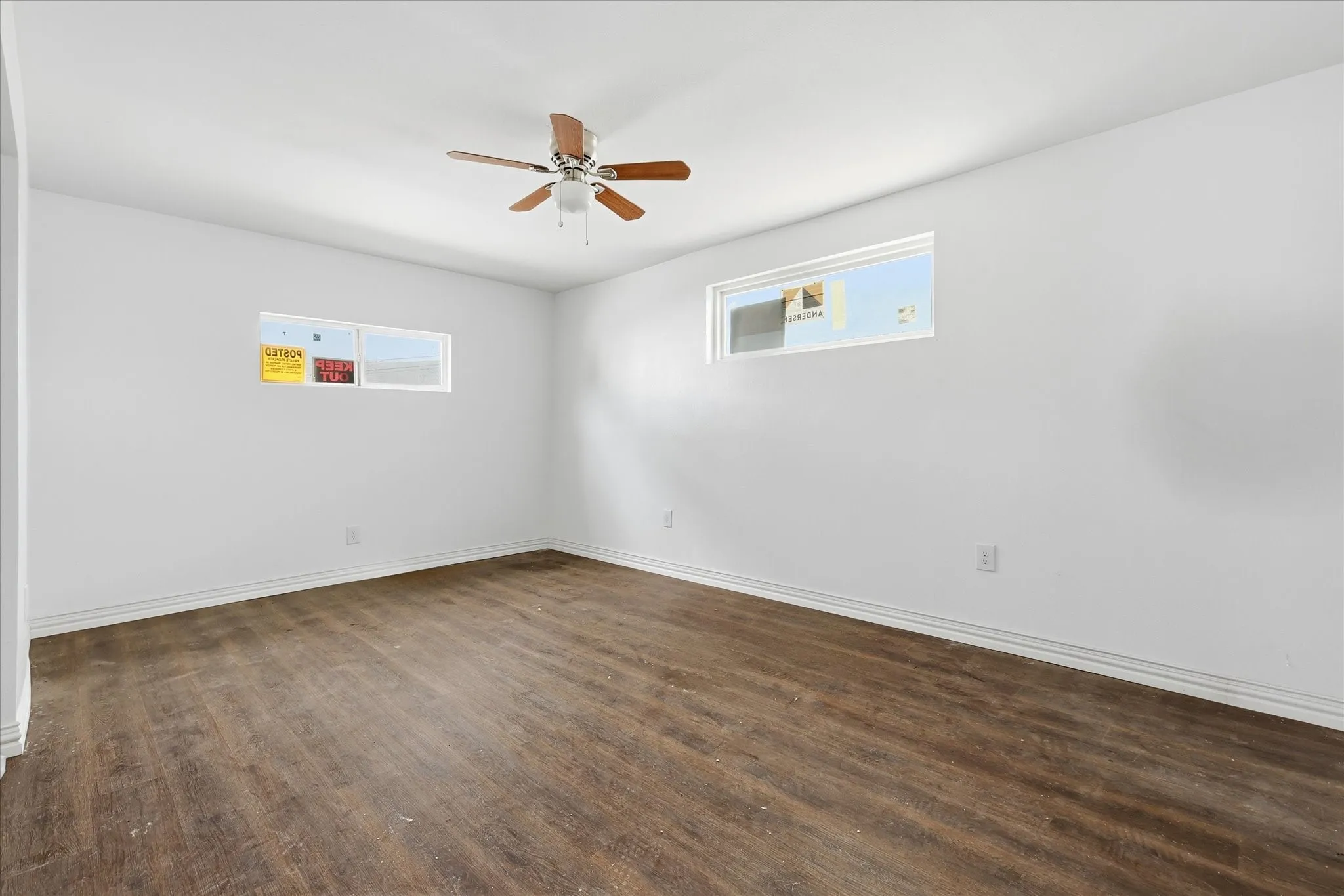 Spacious room featuring wood-finish flooring, white walls, and a ceiling fan
