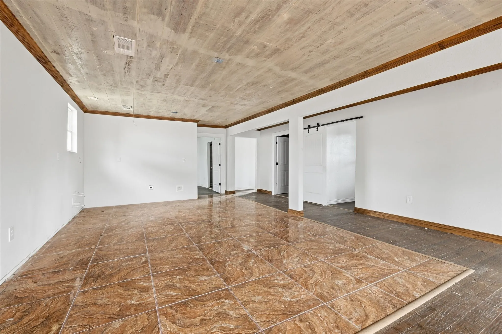 Spacious interior featuring a tiled floor, wood-finish ceiling, white walls, and a barn door