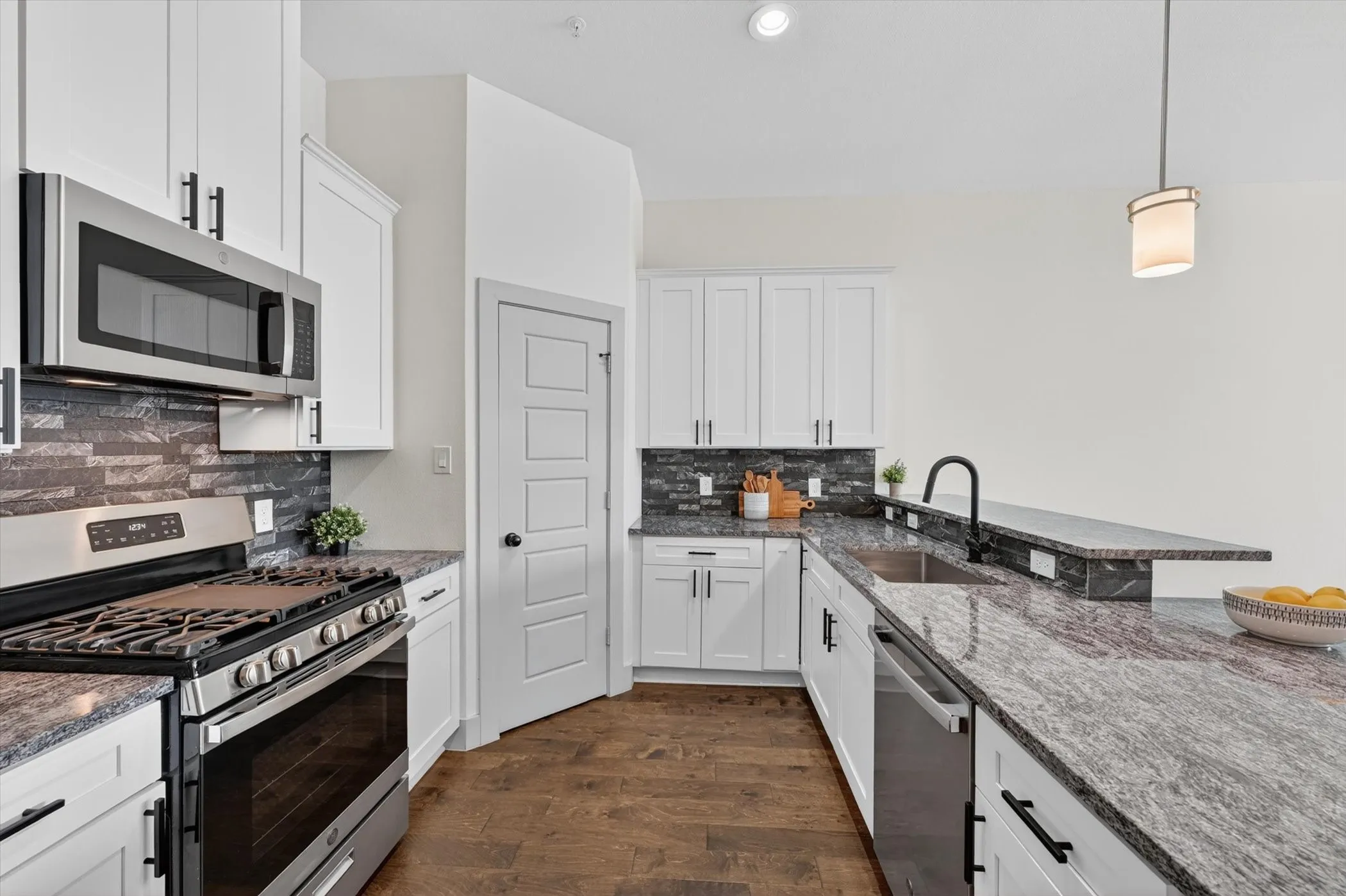 Modern kitchen featuring white shaker cabinetry, stainless steel appliances, dark wood-finish flooring, granite countertops, and a stacked stone-look backsplash