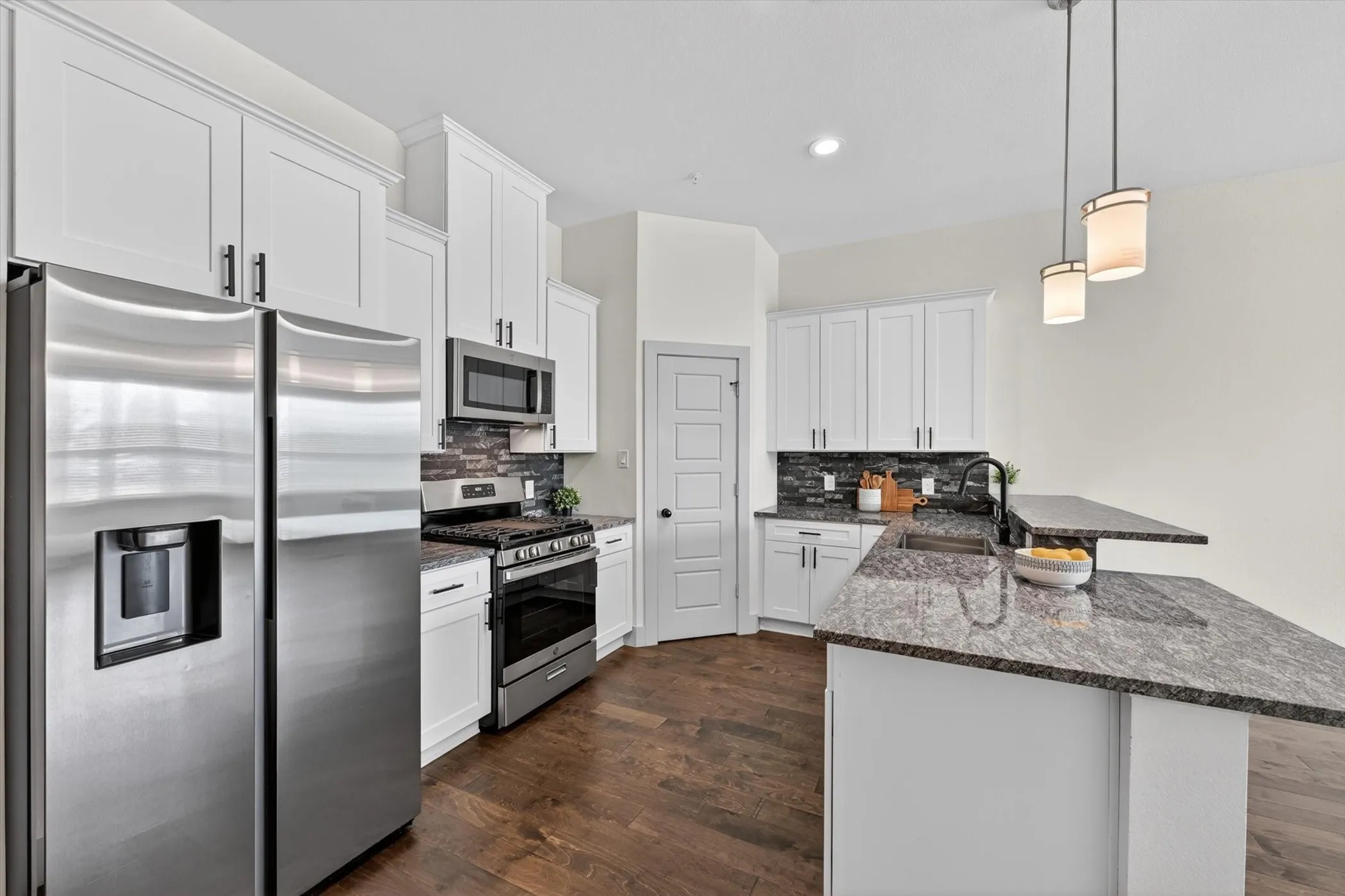Modern kitchen featuring stainless steel appliances, white shaker cabinetry, dark wood-finish flooring, a dark stone countertop, and pendant lighting