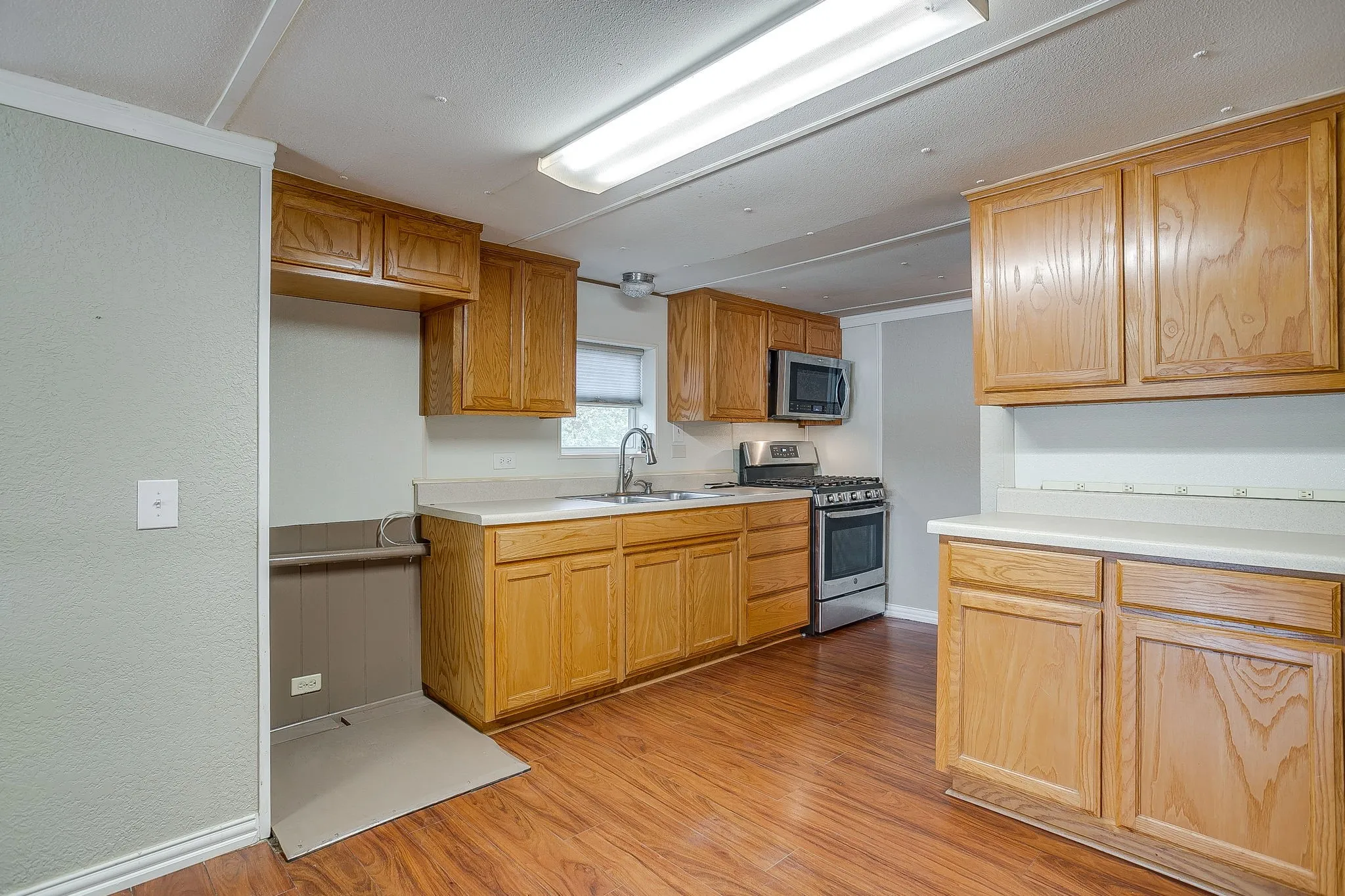 Kitchen featuring wood-finish flooring, wood cabinetry, stainless steel microwave, stainless steel gas range, and a stainless steel sink with a gooseneck faucet
