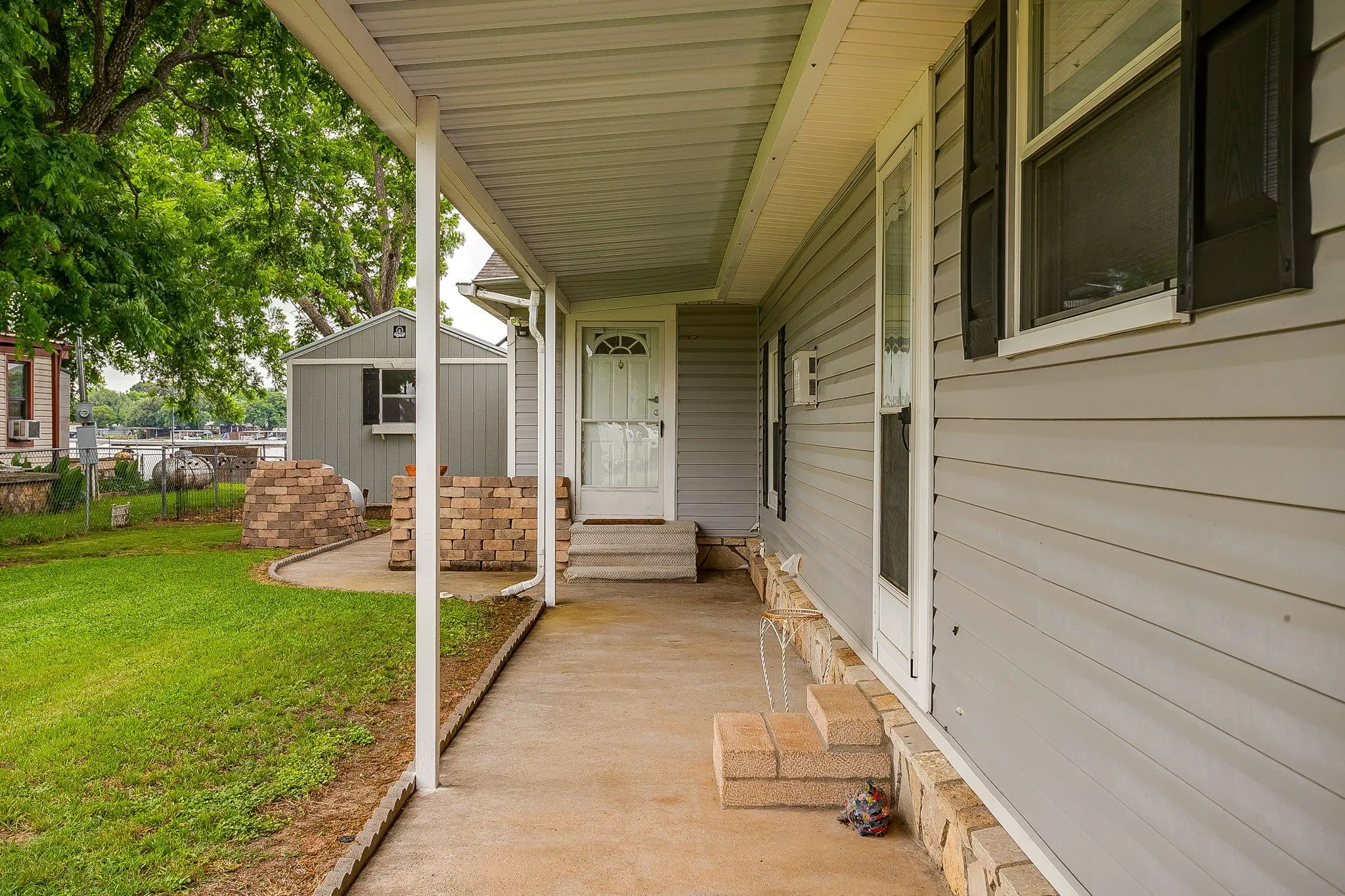 Covered concrete porch with white support columns, gray siding, and dark window shutters