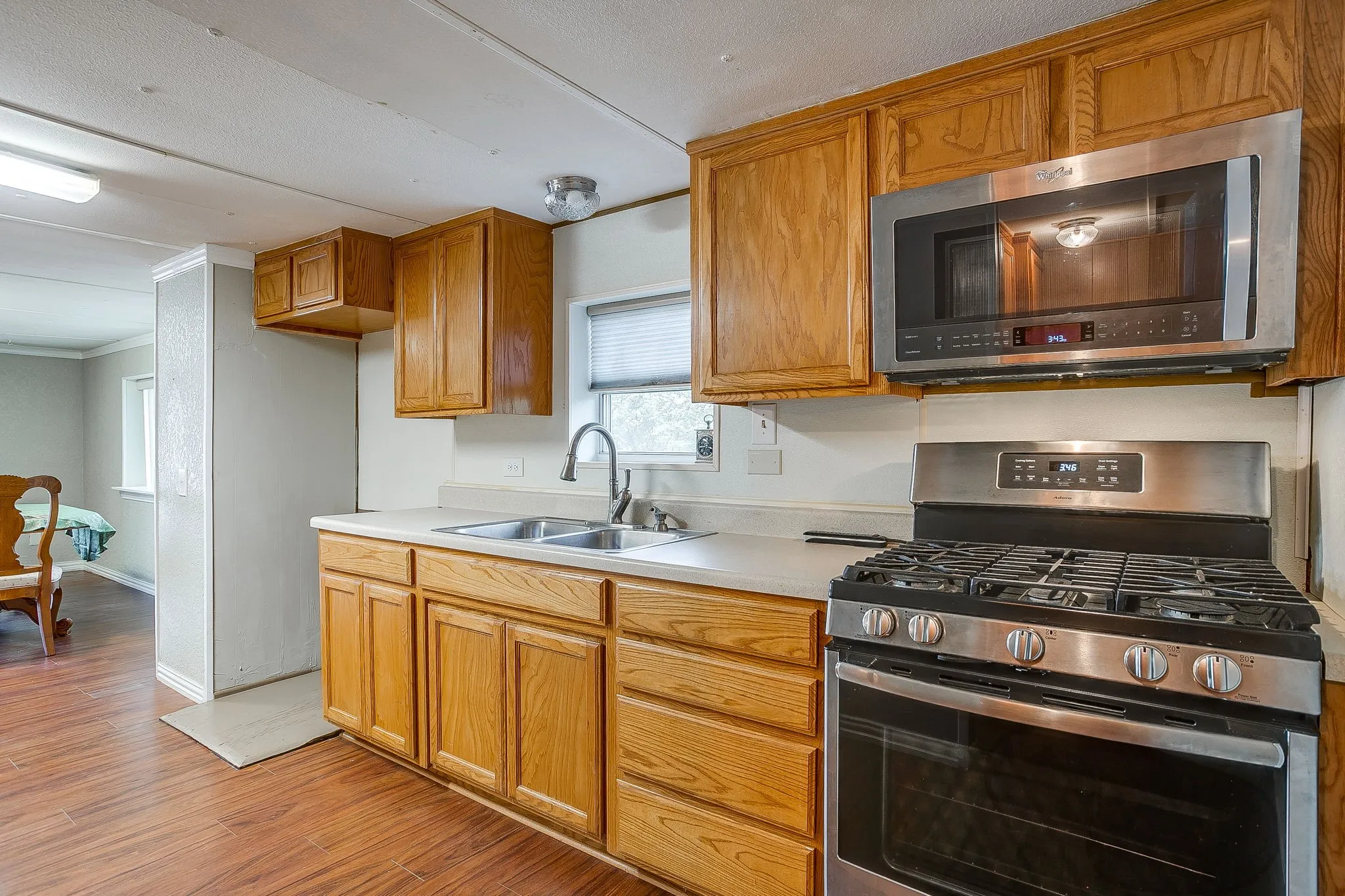 Kitchen featuring wood-finish flooring, light wood cabinetry, stainless steel gas range, stainless steel over-the-range microwave, and a double basin sink