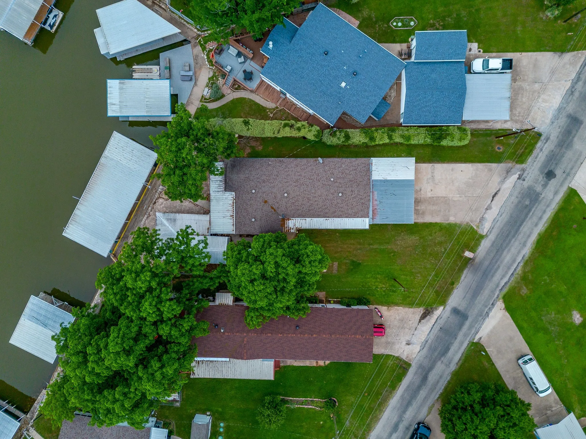 Waterfront property featuring multiple boat slips with covered docks, expansive green lawns, and mature trees