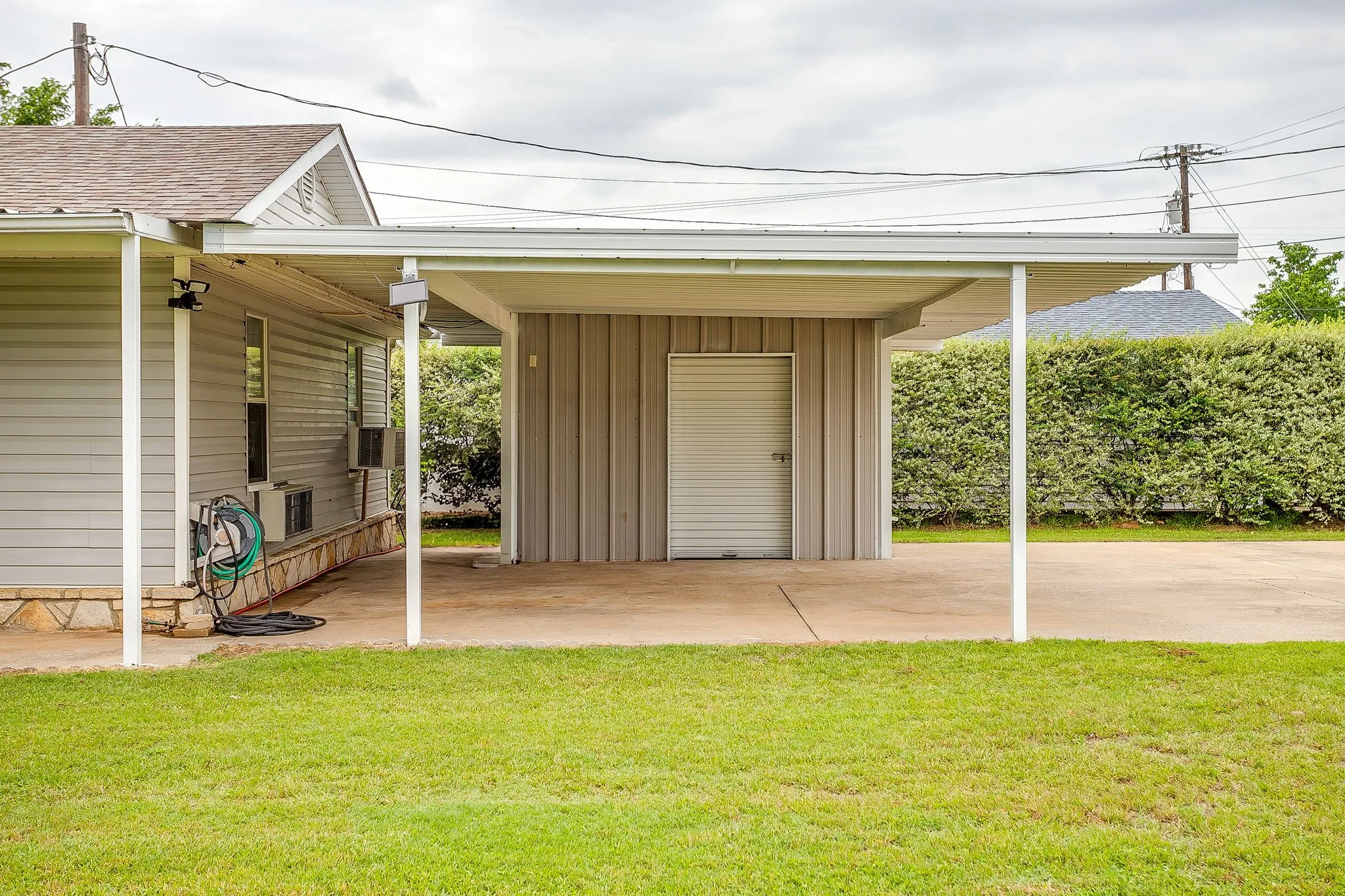 Carport featuring a concrete slab and direct access to an exterior storage room with a roll-up door