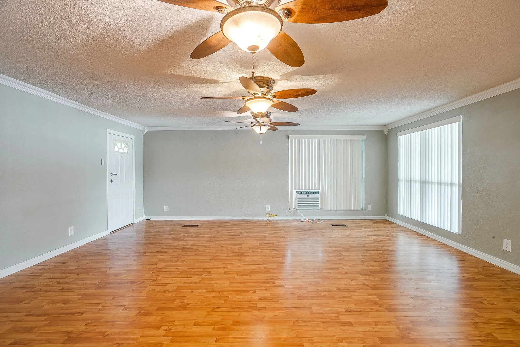 Spacious interior featuring wood-finish flooring, light grey walls, and multiple ceiling fans with integrated lighting
