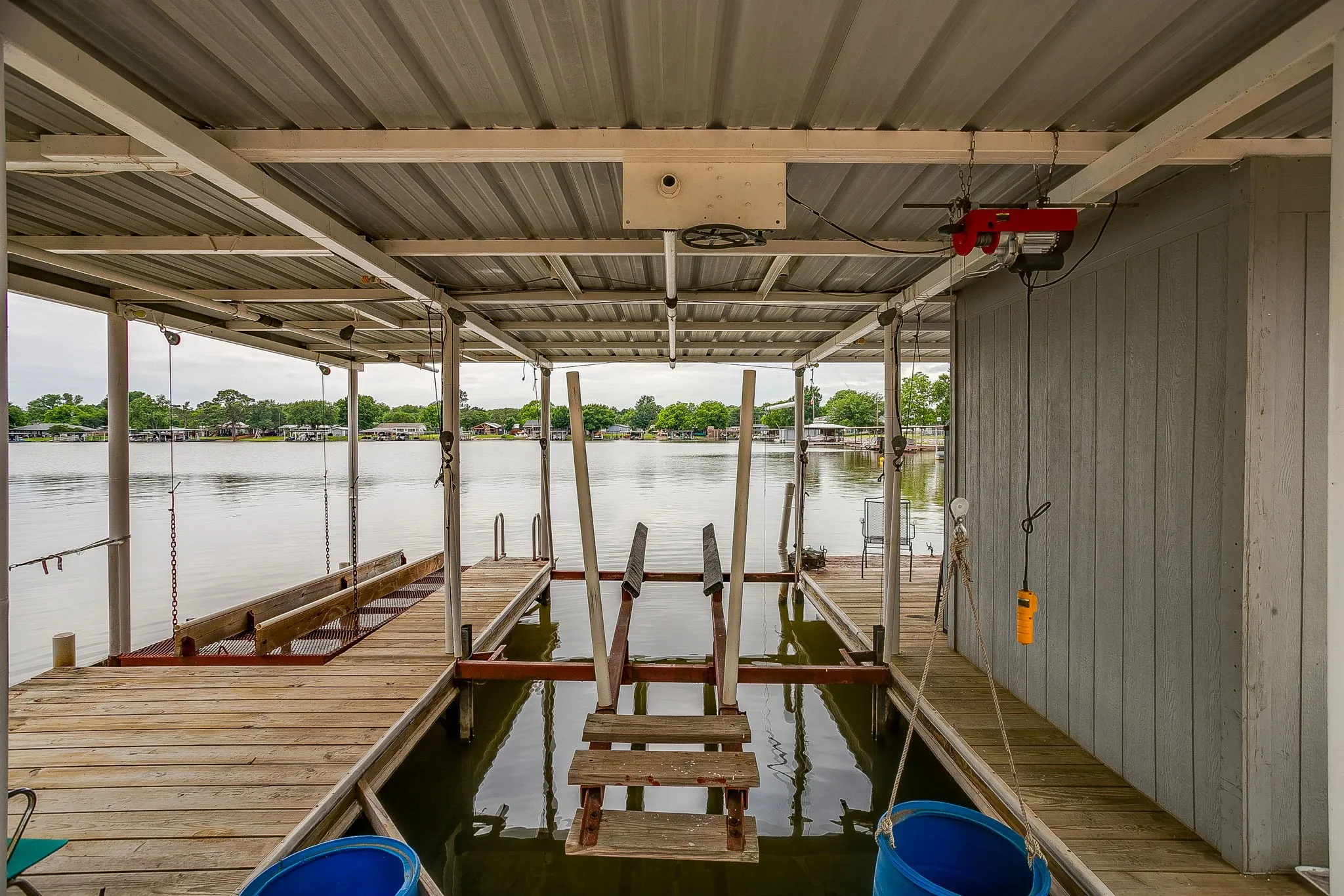 Covered boat dock featuring a metal roof structure, wood plank decking, a boat lift mechanism, and a multi-level water access ladder
