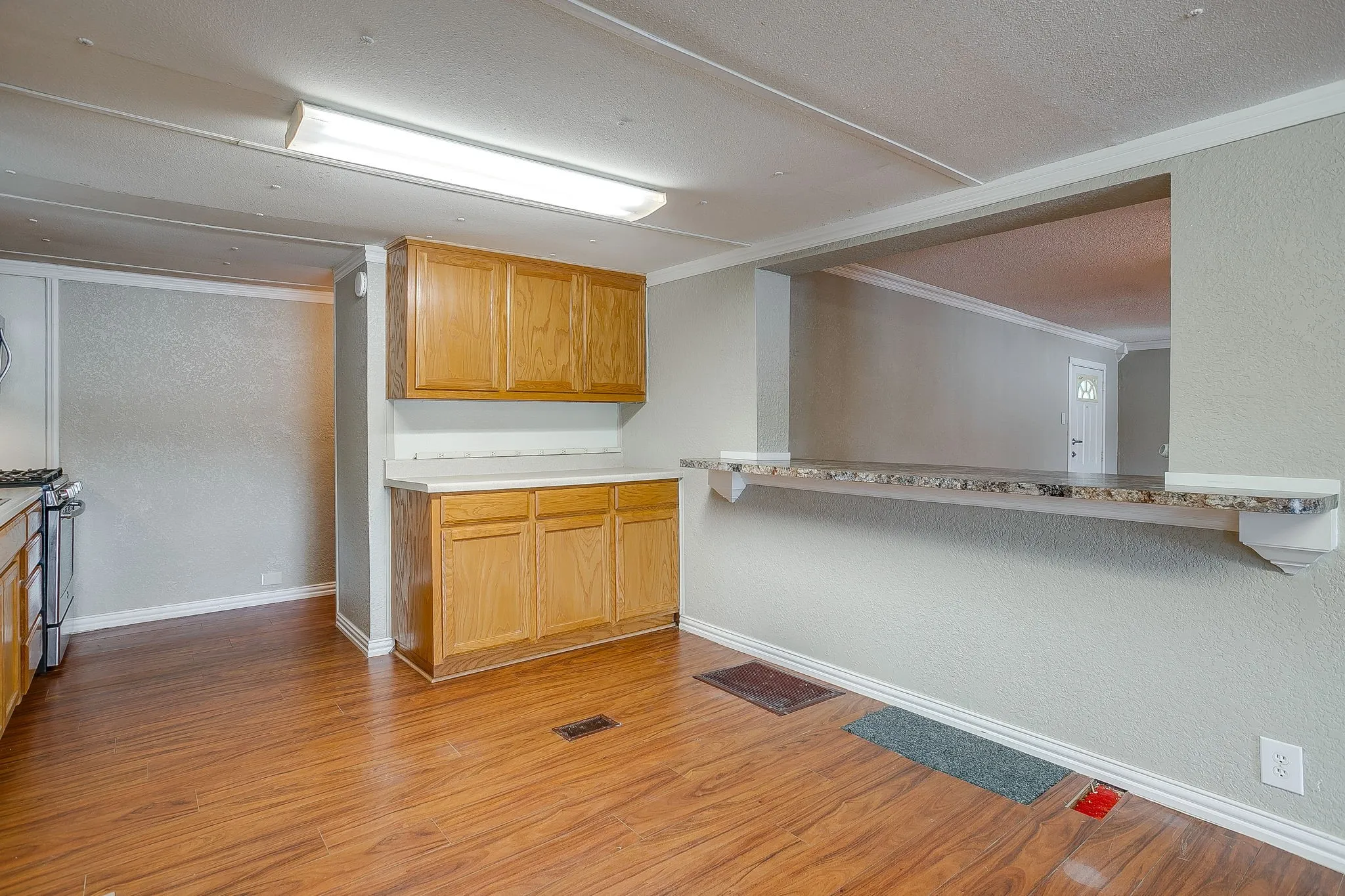 Kitchen space featuring wood-finish flooring, light wood cabinetry, and a pass-through counter with a stone-look surface