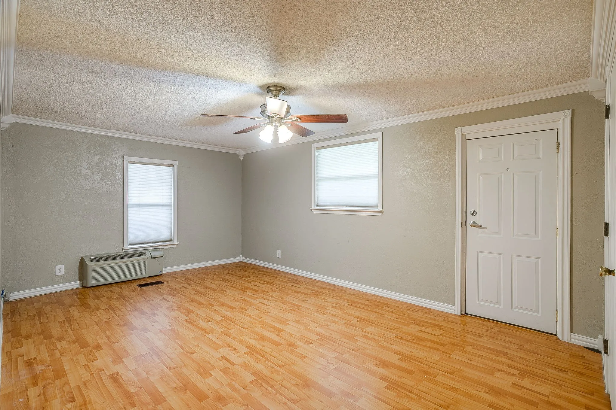 Spacious interior room featuring wood-finish flooring, two windows with blinds, a ceiling fan with integrated lighting, and crown molding