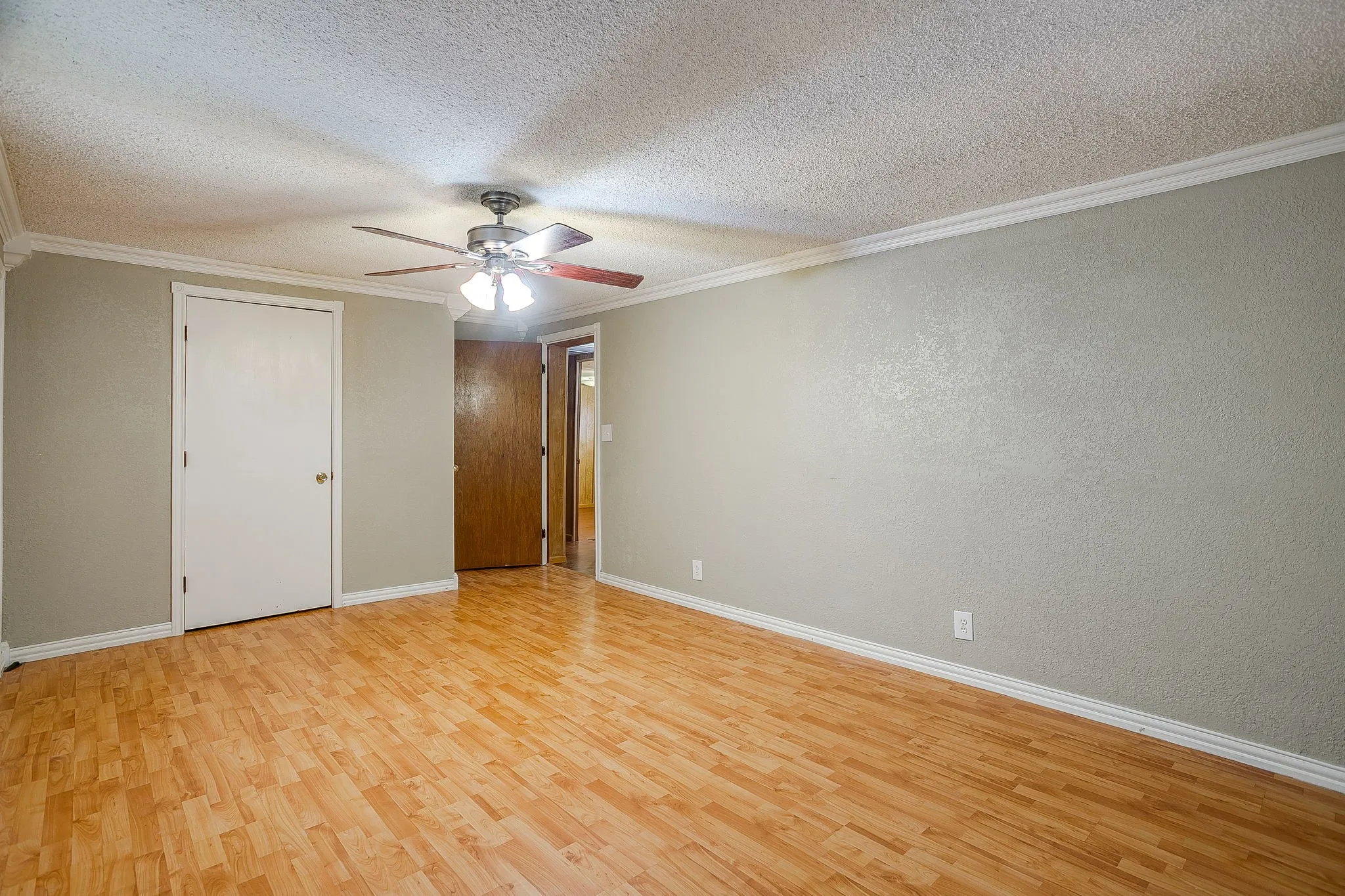 Spacious room featuring wood-finish flooring, a ceiling fan with integrated lighting, two panel doors, and neutral-toned walls with white trim