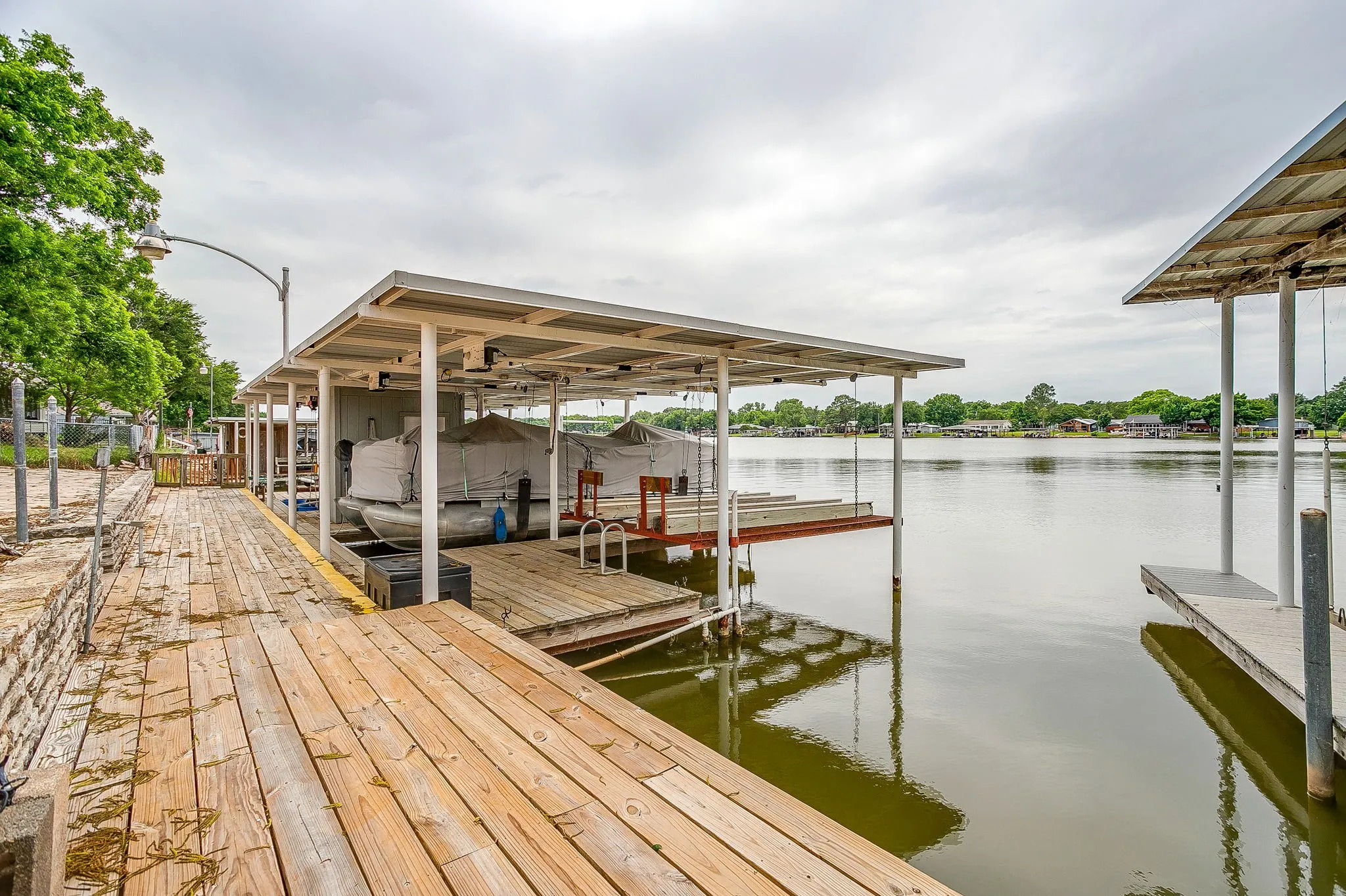 Private boat dock featuring multiple slips with covered roofs, wood decking, and a stone retaining wall