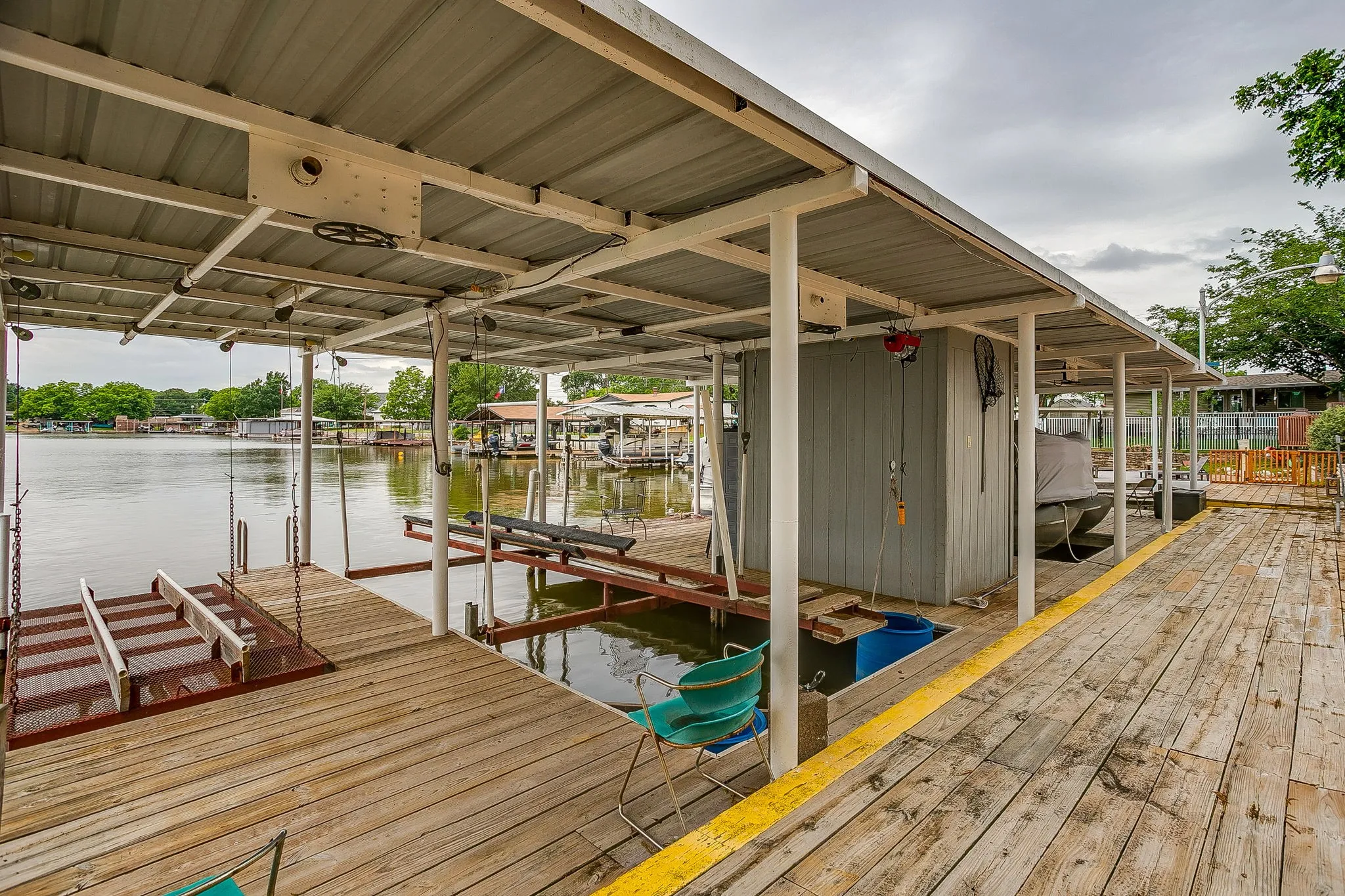 Covered boat dock featuring two boat slips, a storage shed, wood-finish decking, and metal roofing