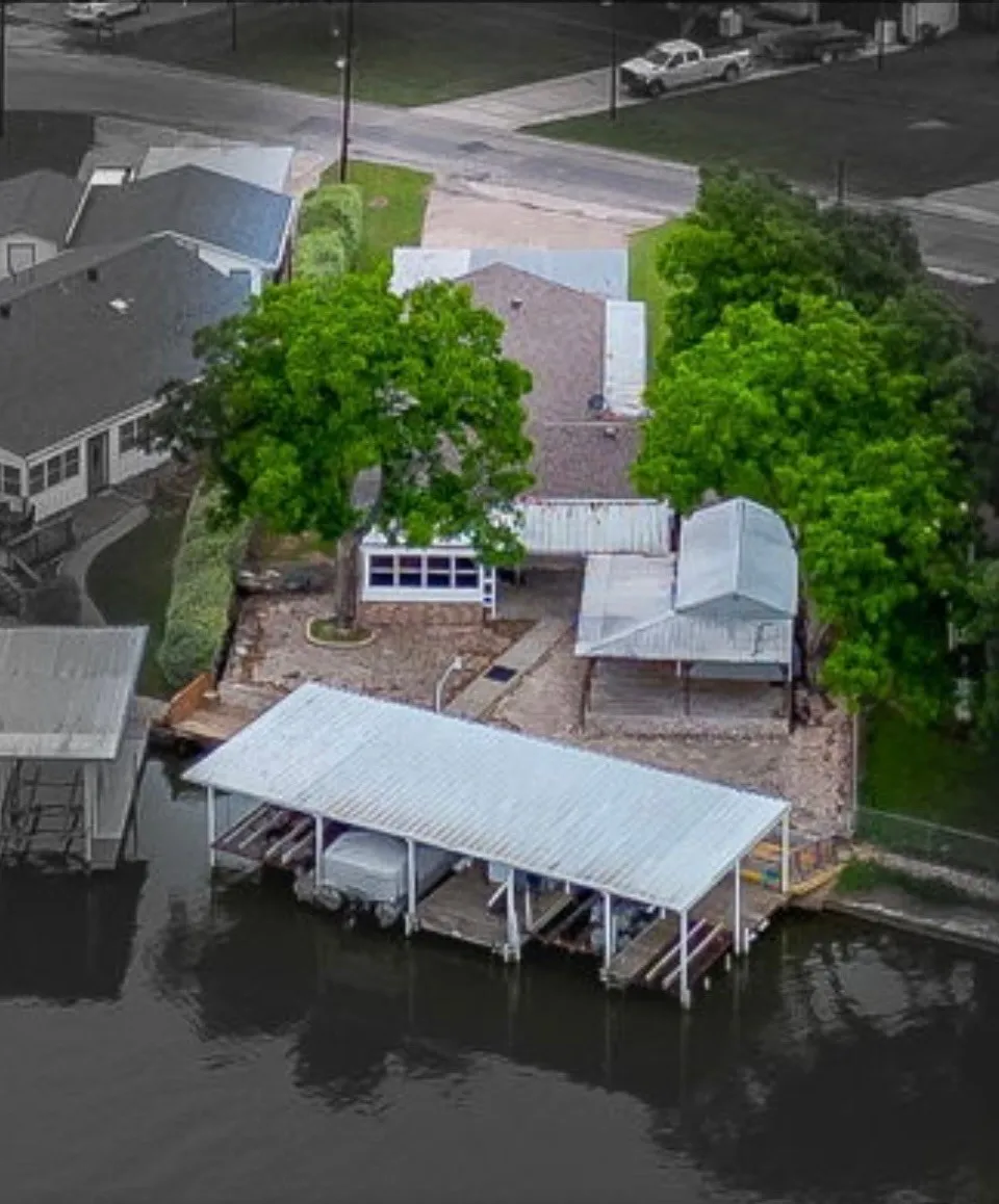 Waterfront property featuring a covered boat dock, additional covered patio, mature trees, and a stone-finish retaining wall