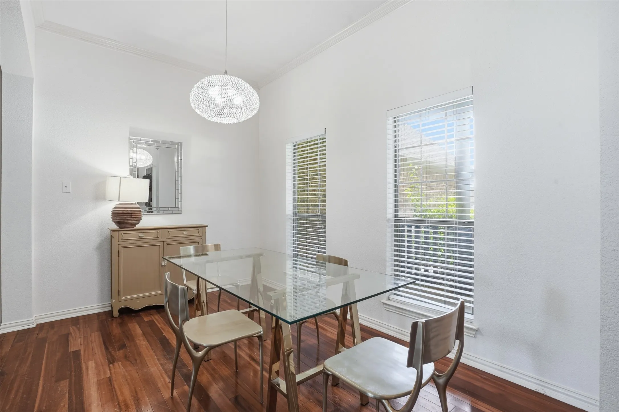 Dining area featuring wood-finish flooring, two large windows with blinds, crown molding, and a modern spherical pendant light fixture