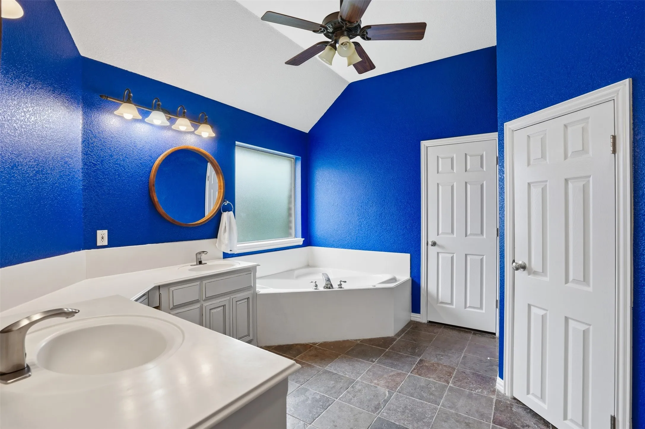 Bathroom featuring a corner soaking tub, dual vanity with undermount sinks, and a ceiling fan