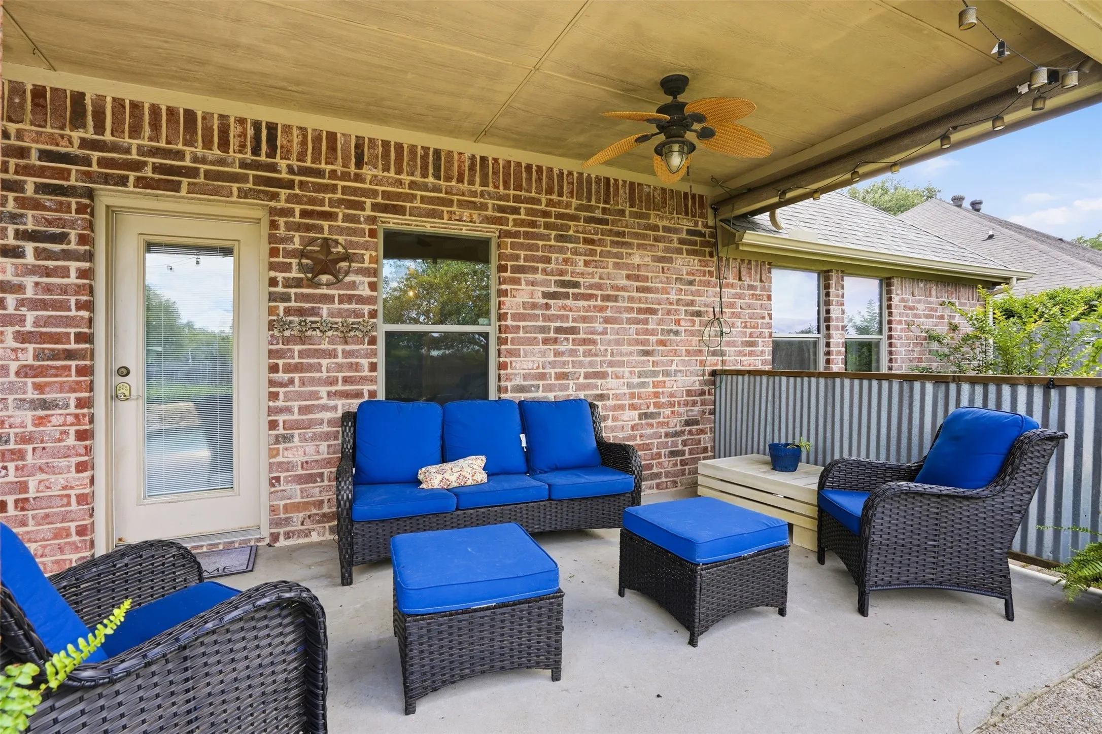 Covered patio featuring a ceiling fan, track lighting, concrete flooring, and a corrugated metal privacy screen