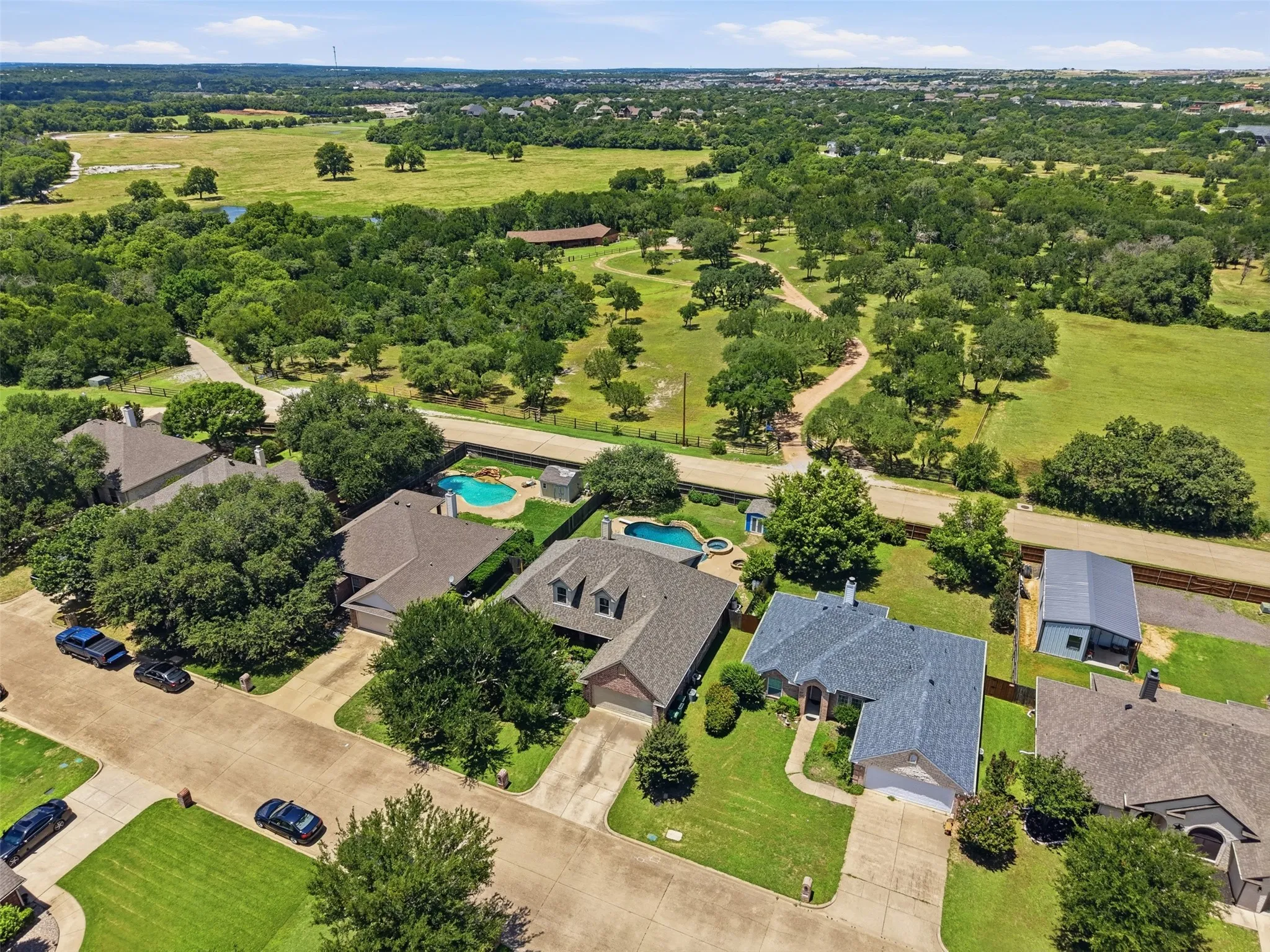 Aerial perspective showcasing a residential area bordered by expansive green fields and mature trees