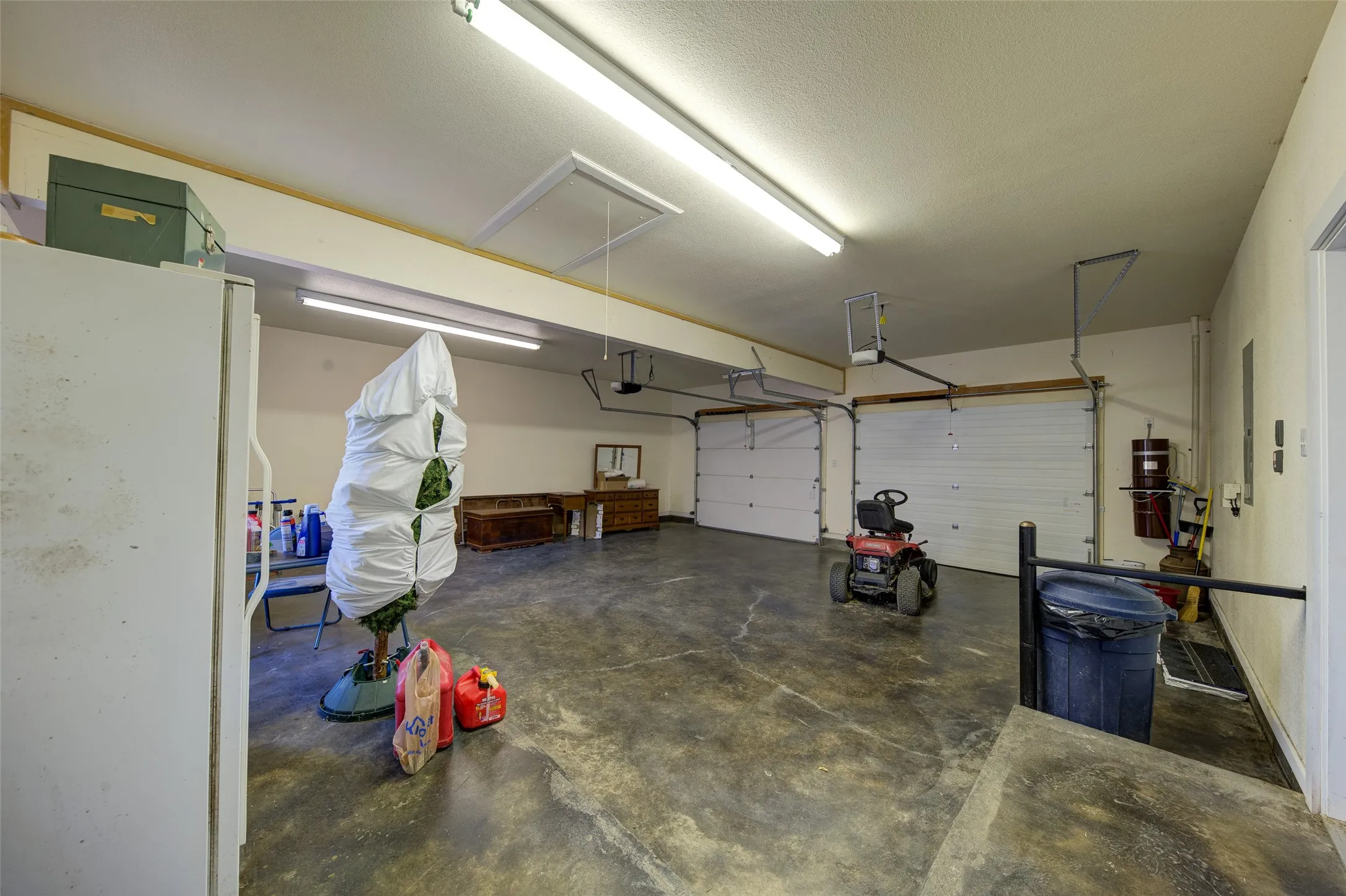 Spacious two-car garage featuring a concrete floor, two white overhead garage doors, and overhead strip lighting