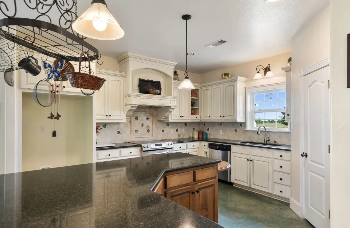 Spacious kitchen featuring an island with a dark countertop, white cabinetry, integrated stainless steel appliances, and a decorative tile backsplash