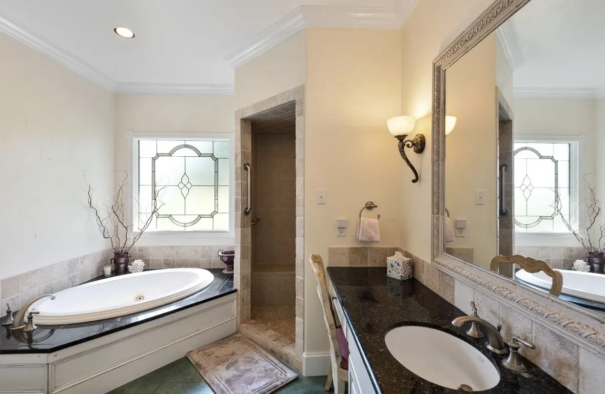 Expansive bathroom featuring a built-in soaking tub with a dark stone surround and decorative stained glass window