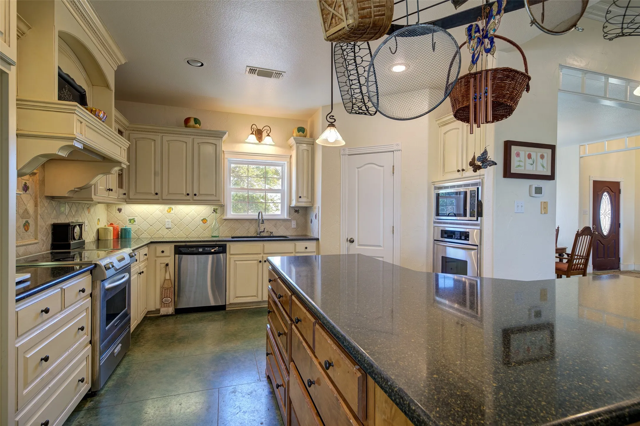 Spacious kitchen featuring a large island with dark stone countertop, light-toned cabinetry, stainless steel appliances, a tiled backsplash, and recessed lighting