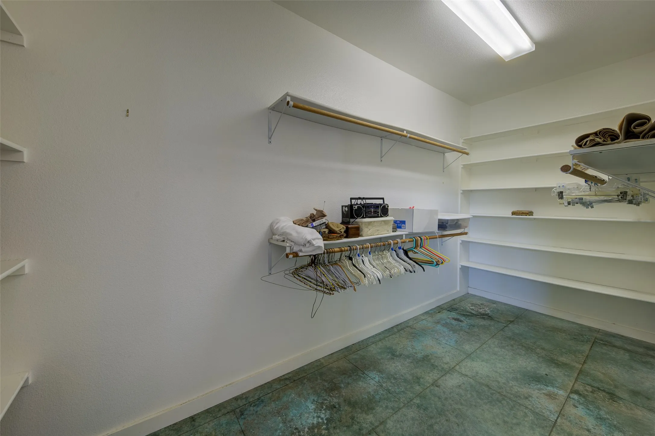 Spacious closet featuring multiple white shelving units and hanging rods, complemented by a distressed concrete floor
