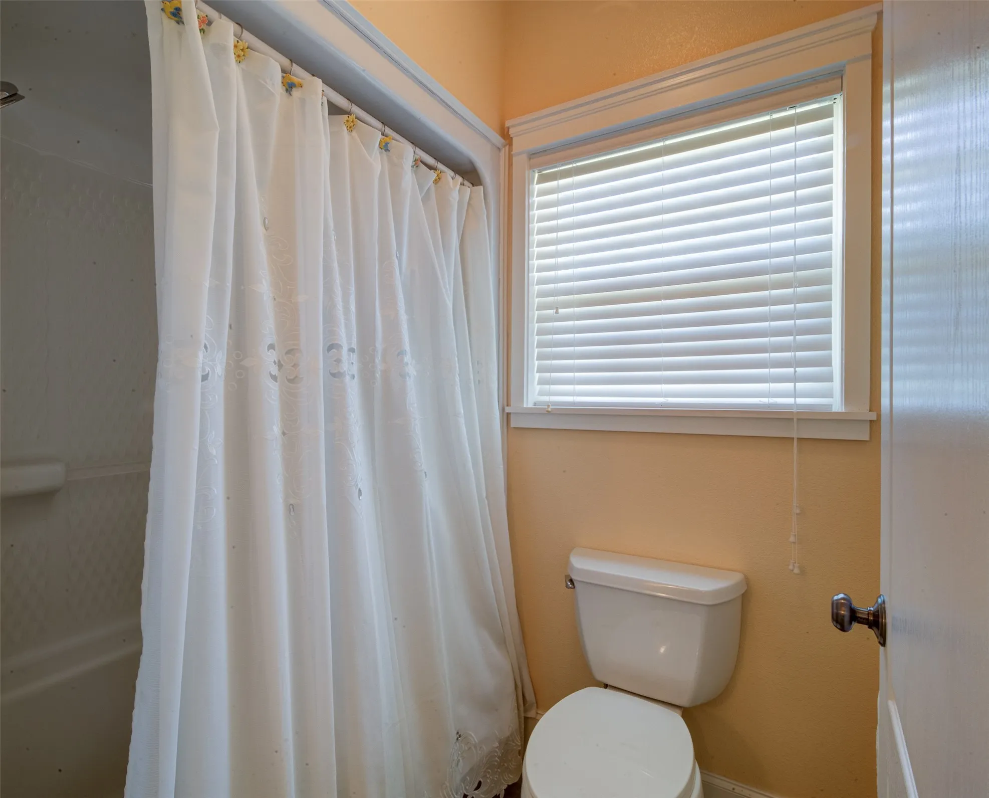 Bathroom featuring a window with white blinds, a toilet, a shower/tub combination with a shower curtain, and a painted wall finish