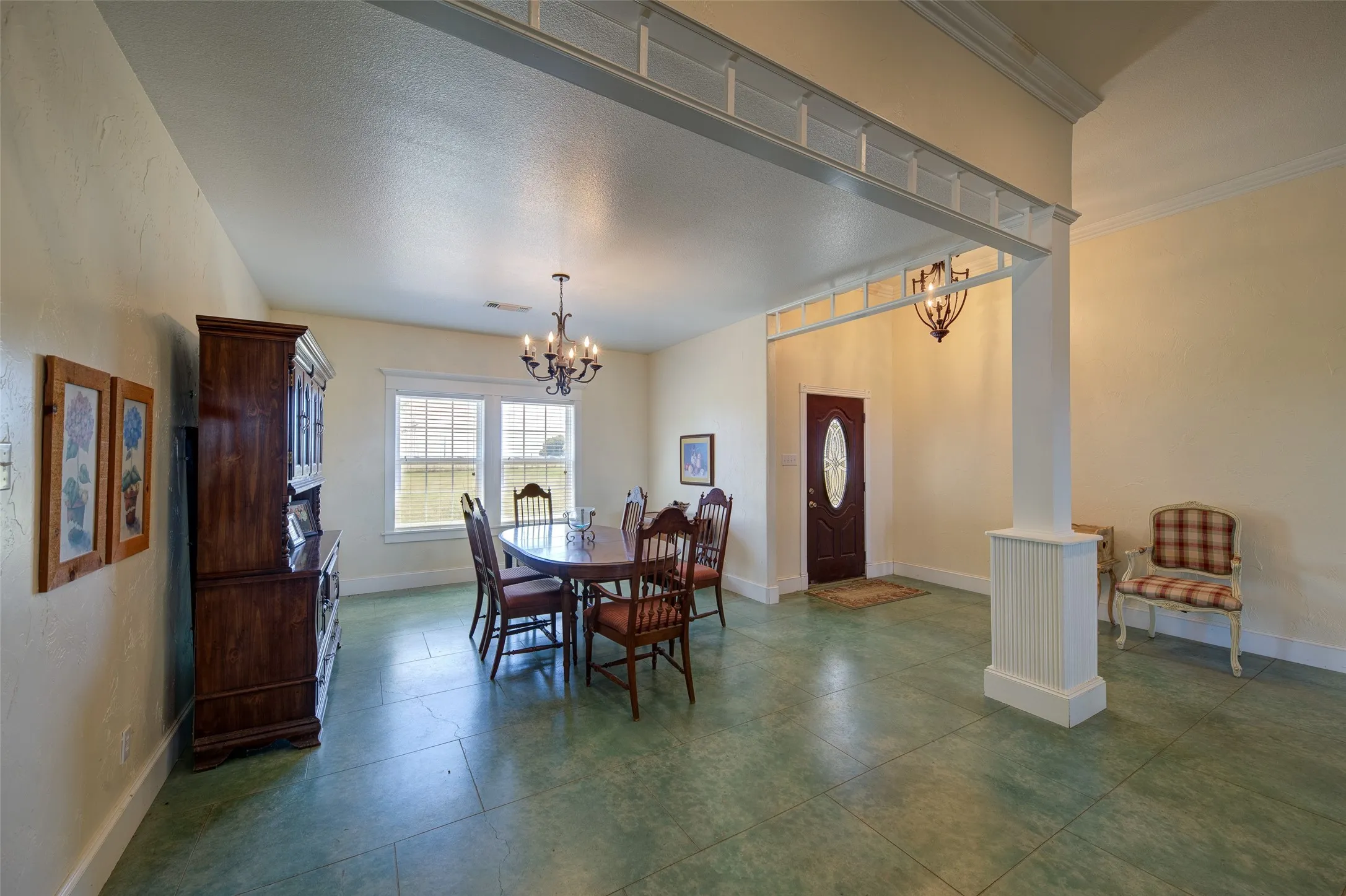 Spacious interior featuring a decorative support column, green-toned tile flooring, and a dark wood-finish entry door with an oval glass insert
