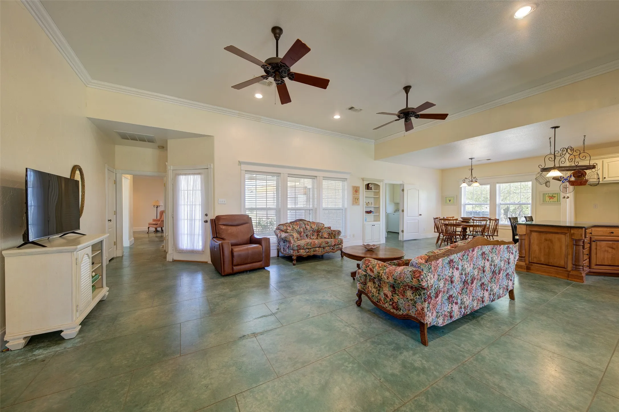 Open-concept interior featuring expansive concrete-look flooring, multiple ceiling fans, and crown molding